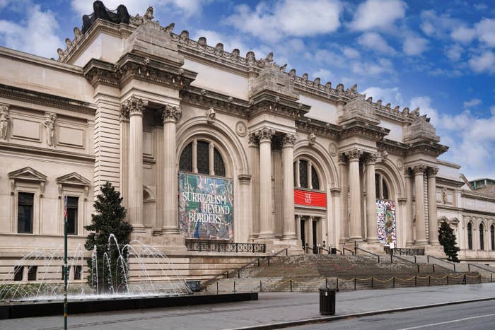 The facade of the Metropolitan Museum of Art with banners displaying exhibition titles, set against a clear sky