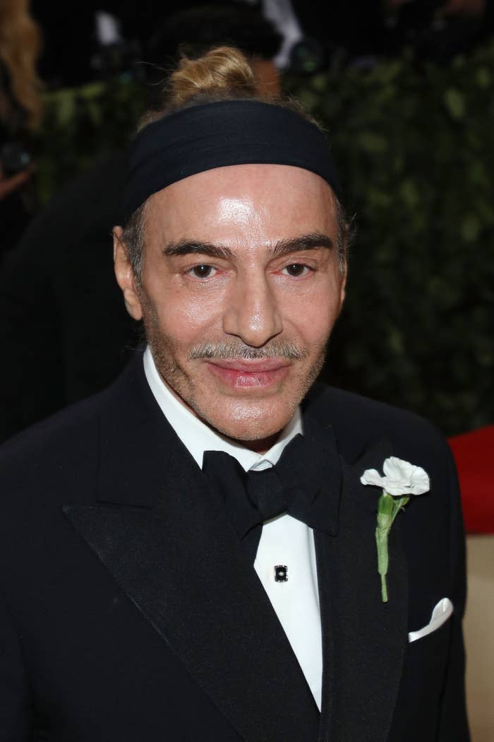 Person in formal black tuxedo with bow tie, wearing a black headband, at an event. White flower on the lapel