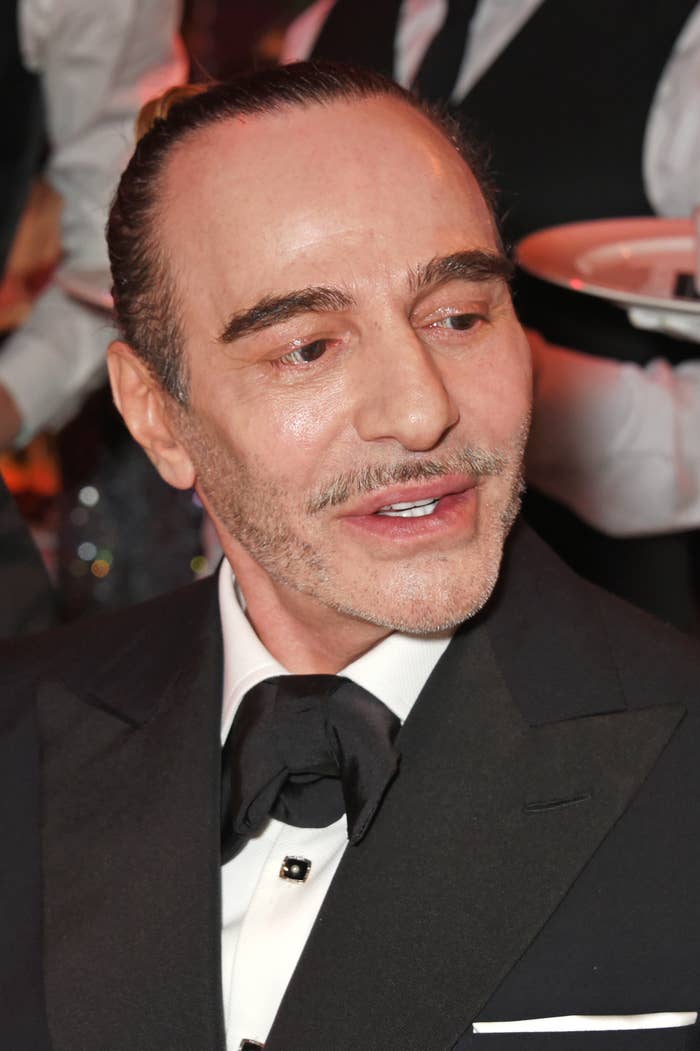 A person in formal attire with slicked-back hair and a black bow tie at an event