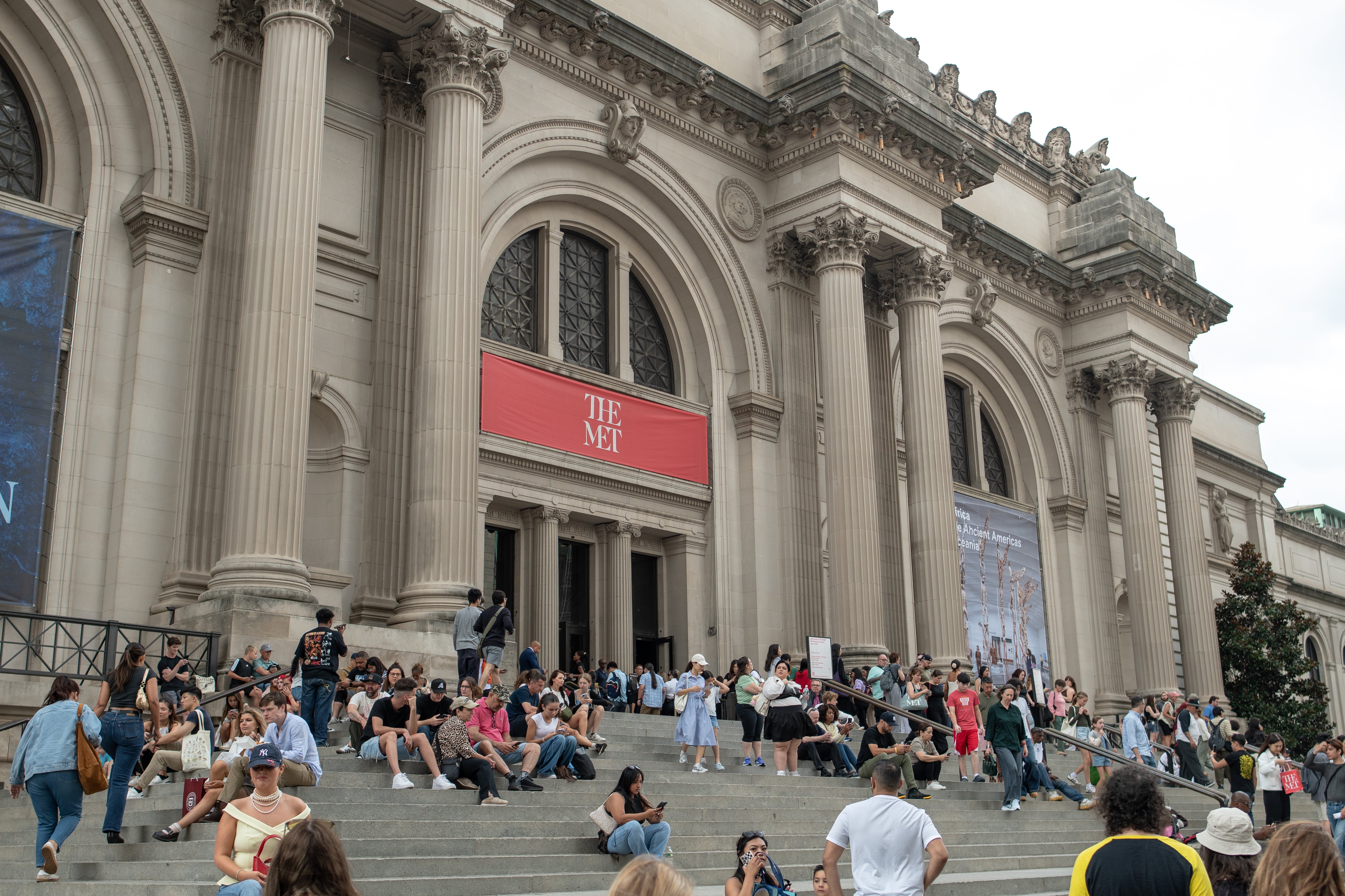 Folk som sitter og går på trappene utenfor The Met, et historisk museum med storslåtte søyler og bannere