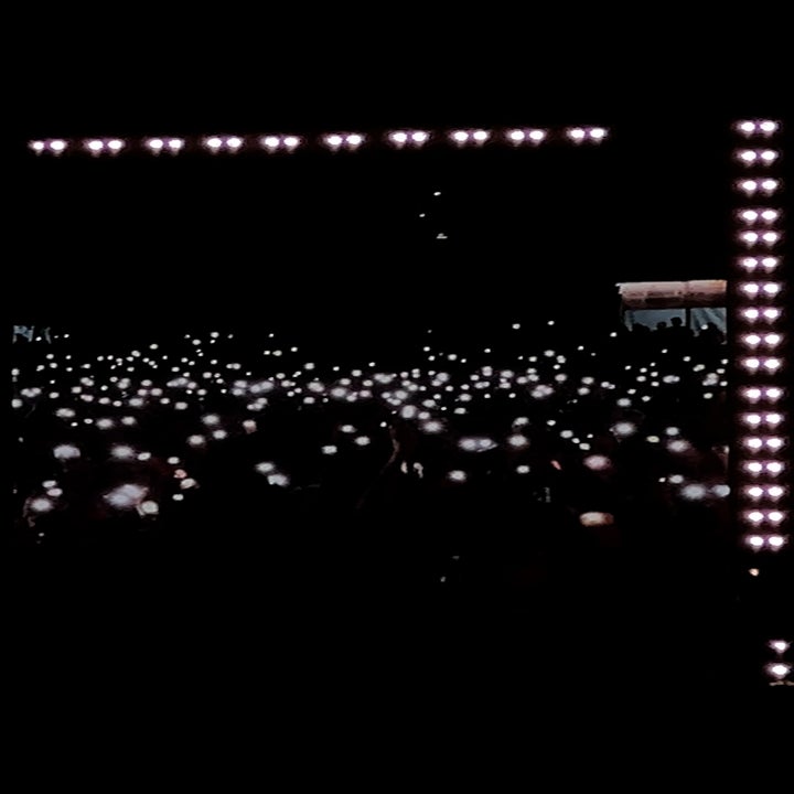 Audience members at a concert hold up phones with lights, creating a sea of glowing dots in the dark