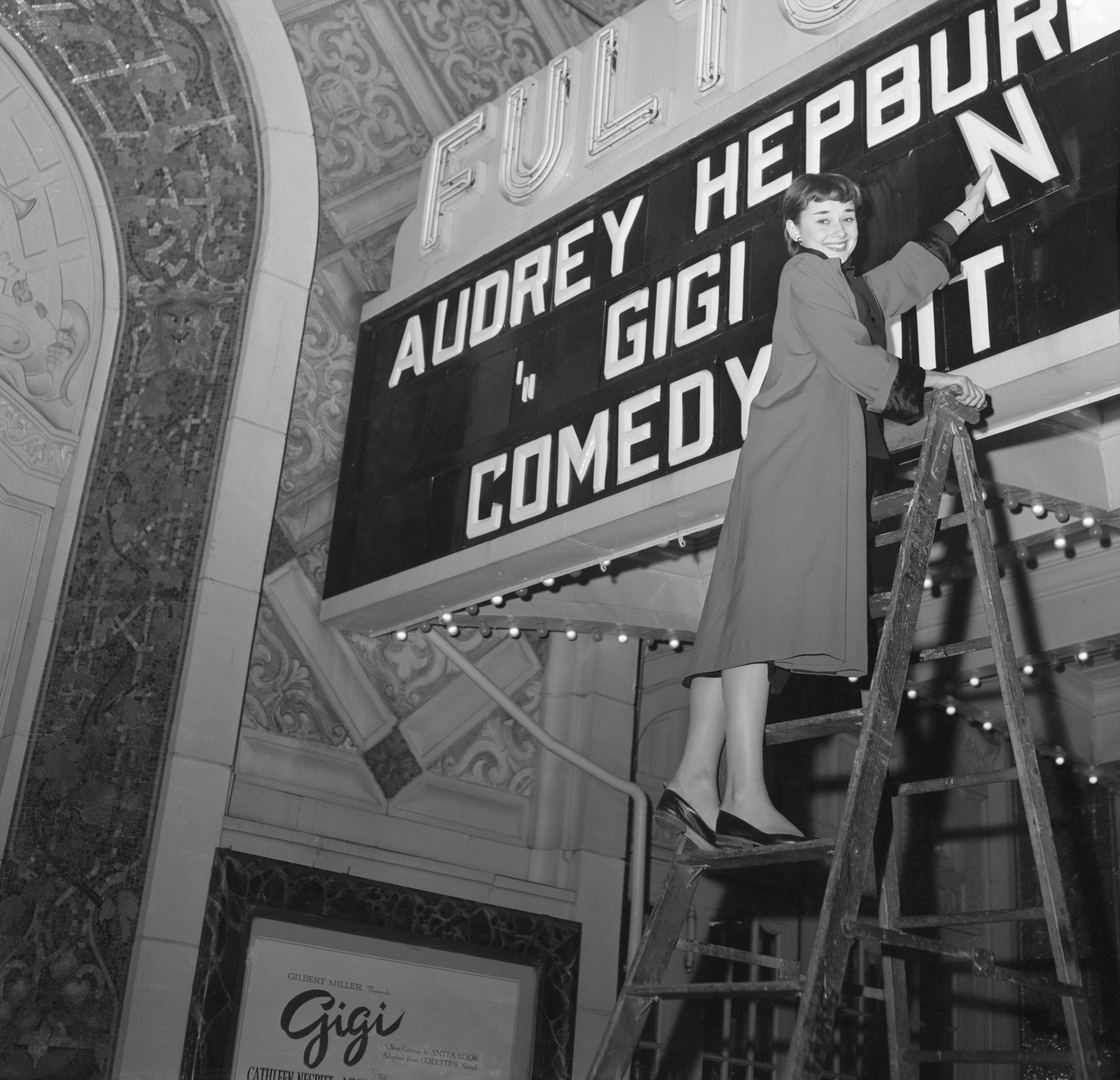 Audrey Hepburn on a ladder adjusting lights on a vintage theater marquee for "Gigi"