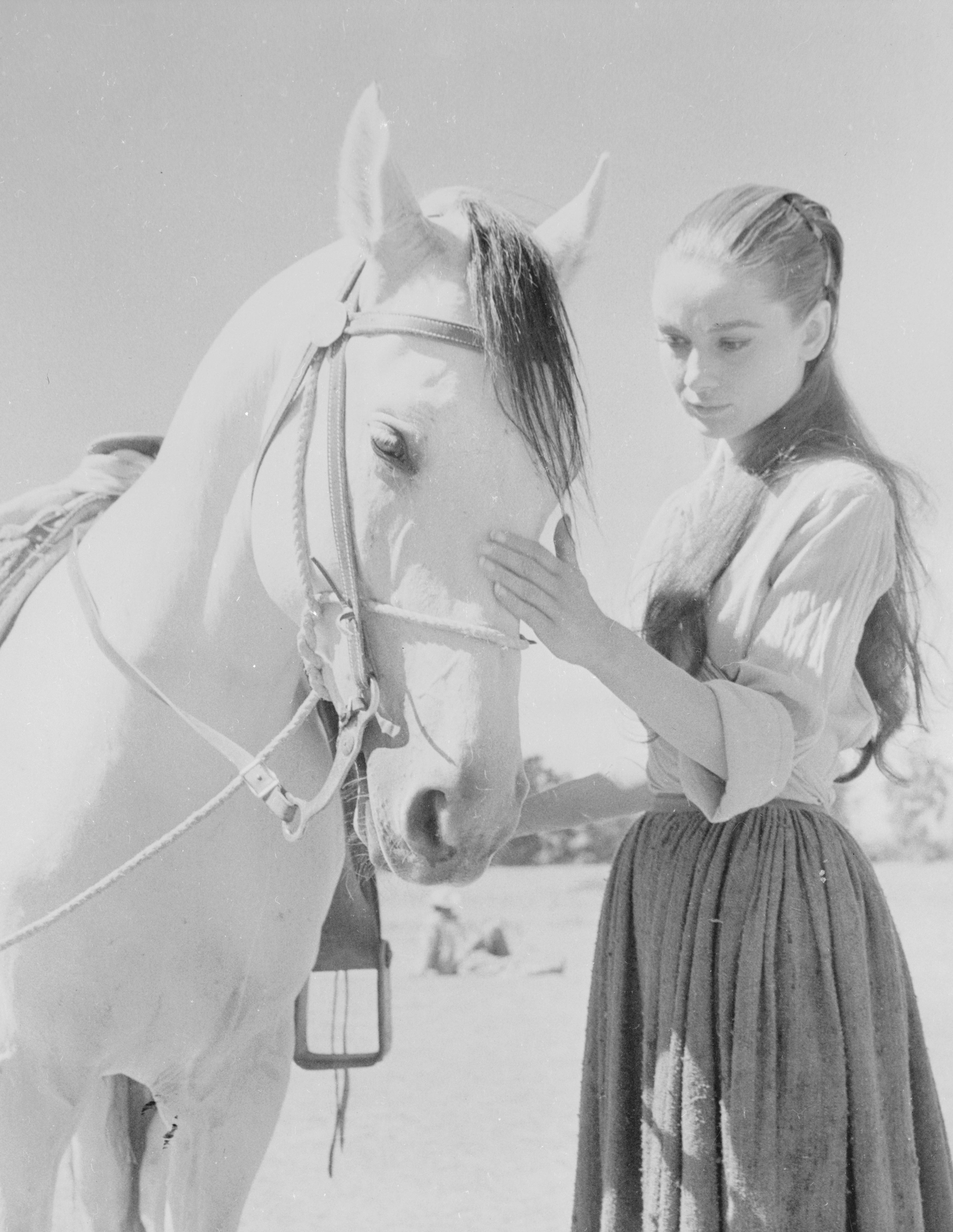 Audrey Hepburn gently touches a horse's face, wearing a simple blouse and long skirt, creating a serene and intimate moment