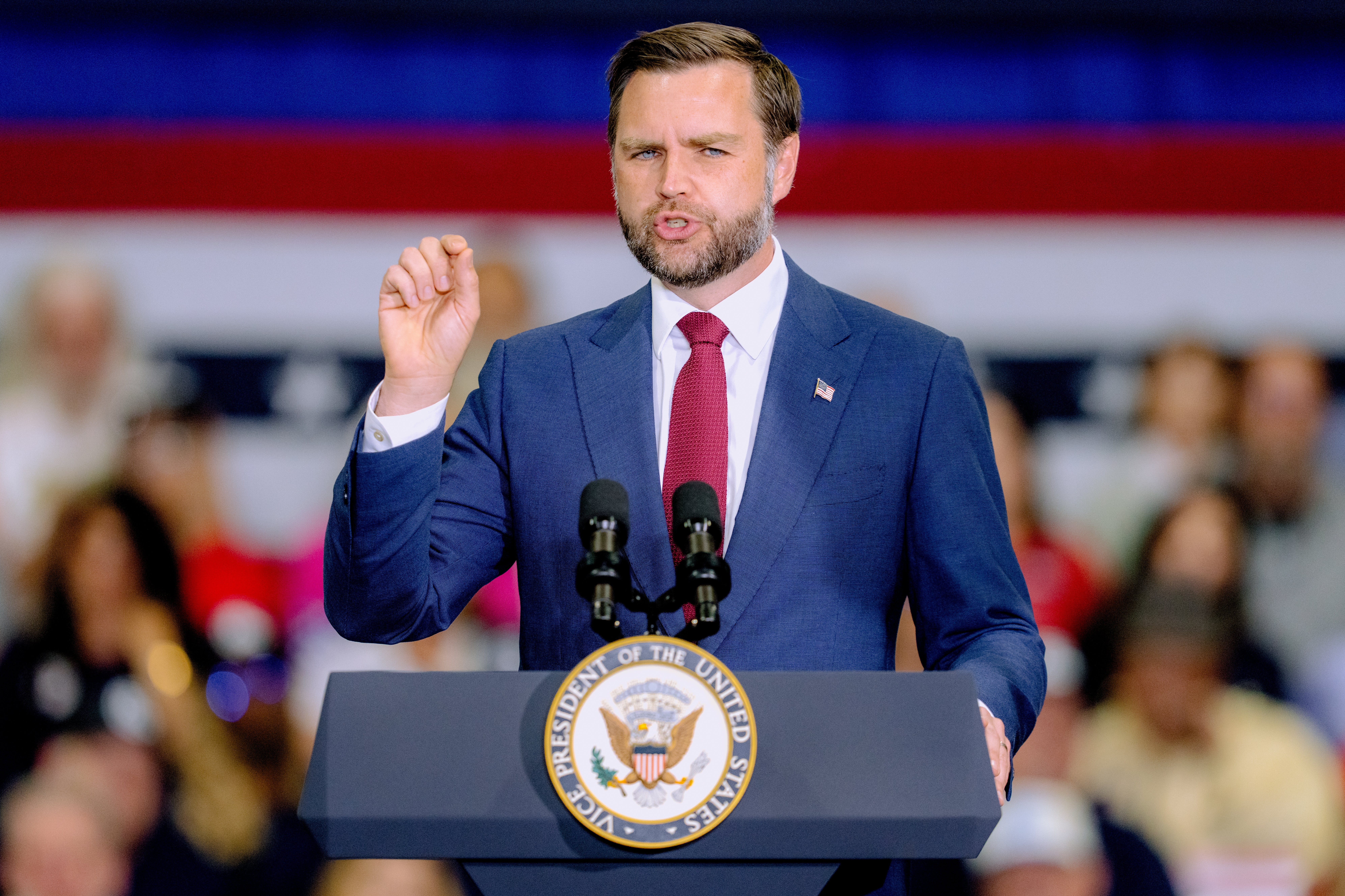 En person i dress snakker lidenskapelig ved et podium med presidentseglet og henvender seg til et publikum