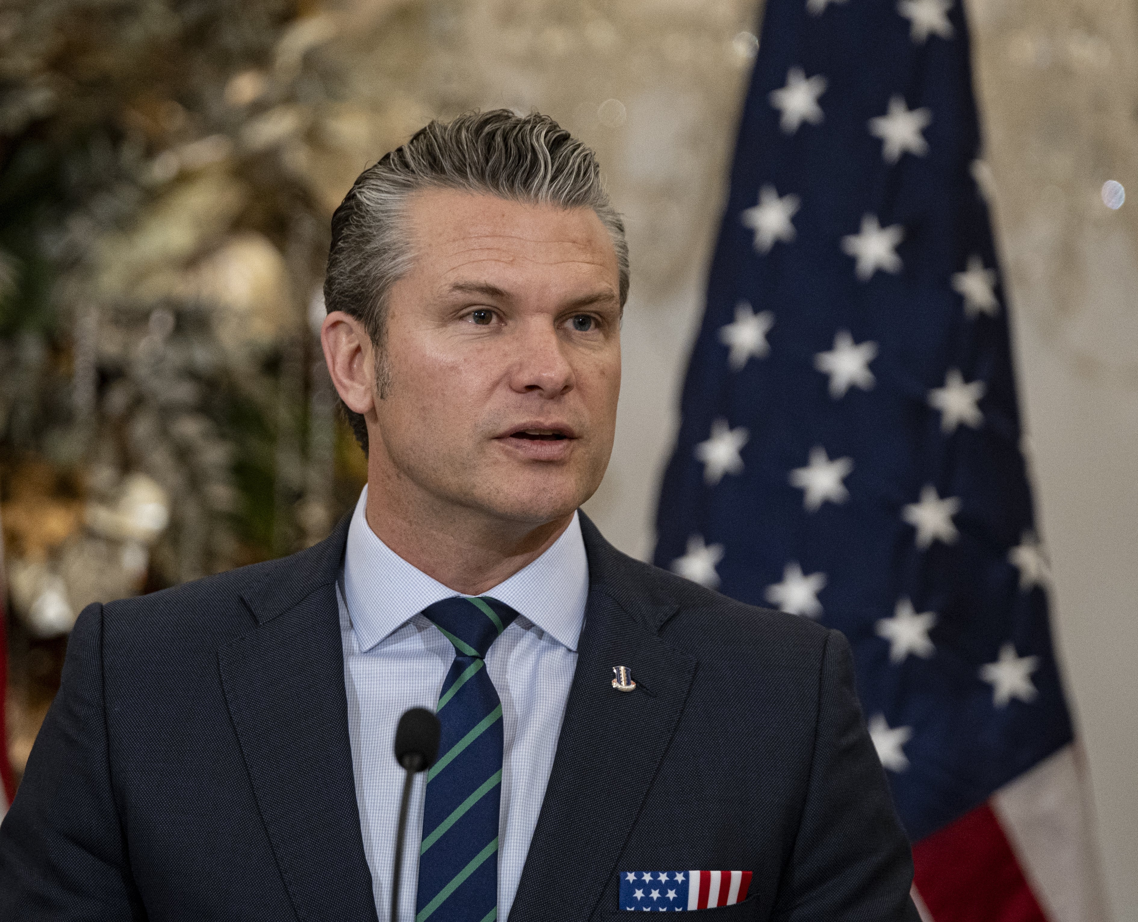 Person som snakker, iført en dress med en amerikansk flaggnål. Et amerikansk flagg er i bakgrunnen