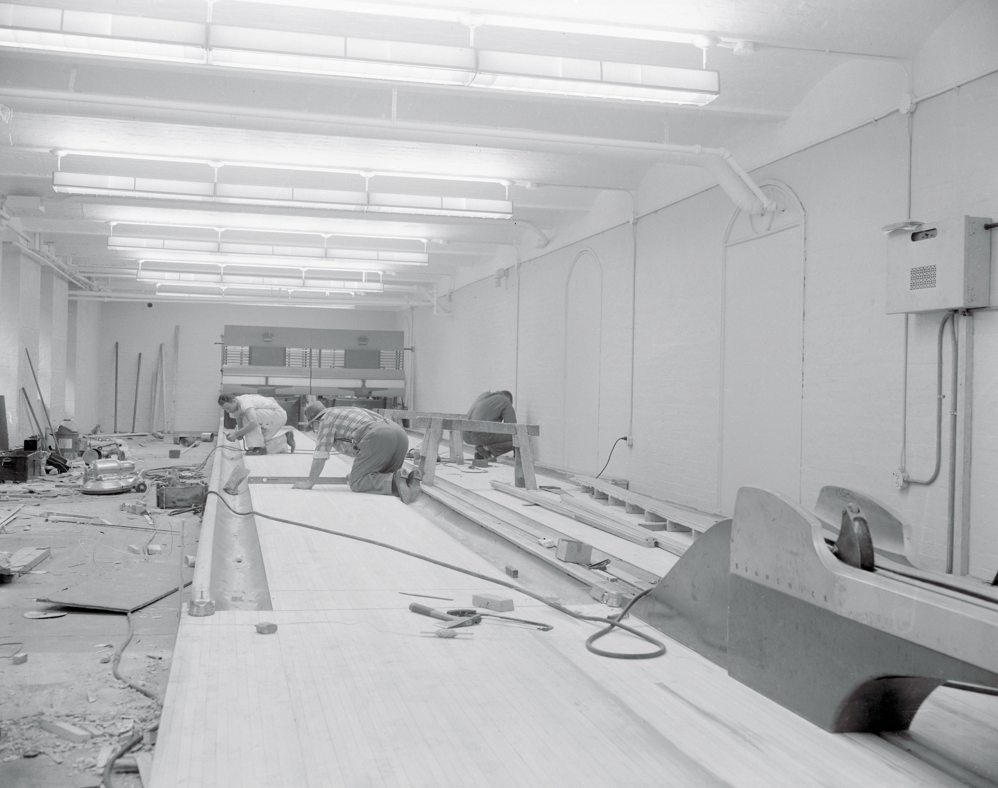 Workers deconstructing a bowling alley lane in an indoor space inside the White House, with tools and materials scattered around