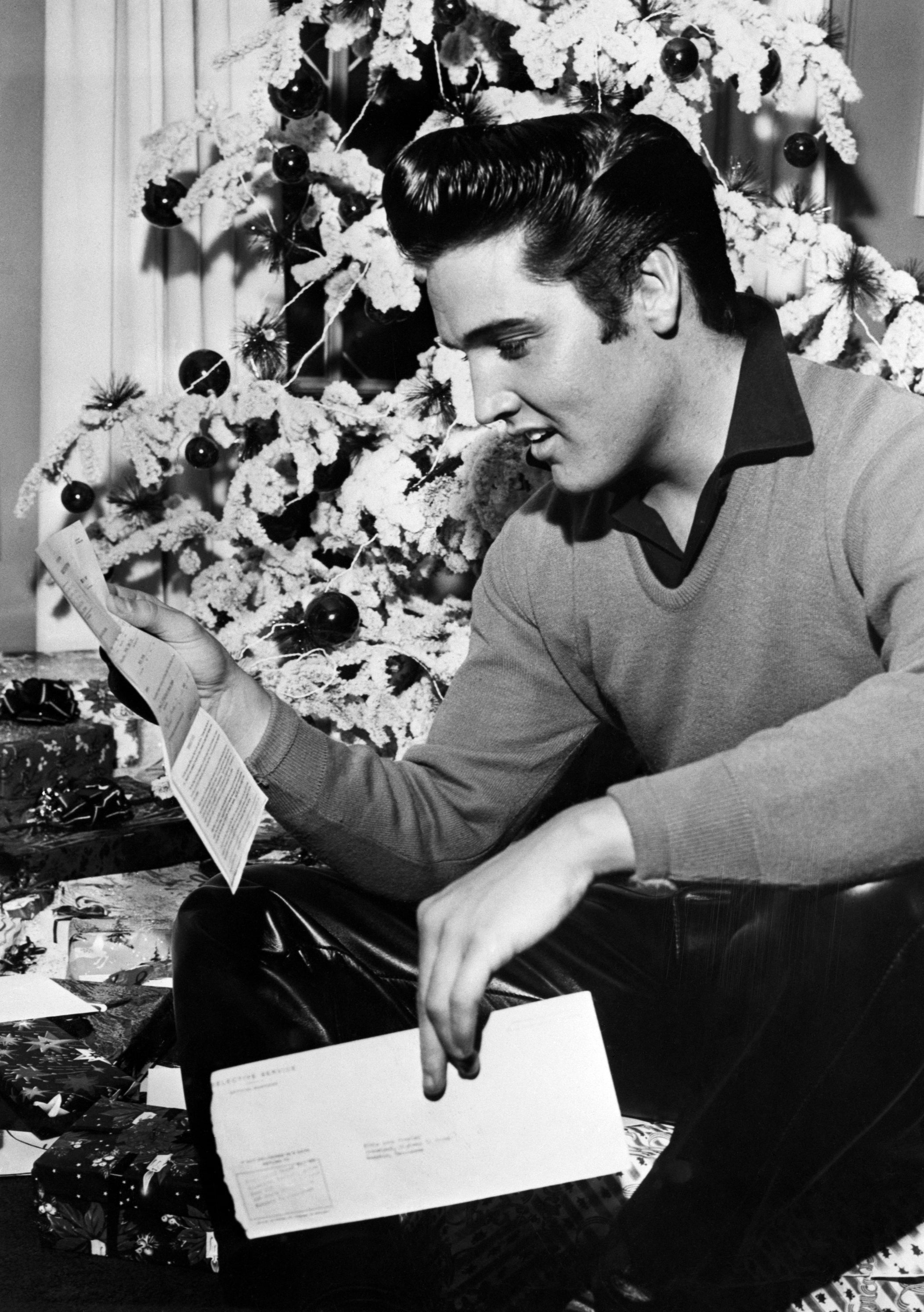 Elvis reading a letter by a decorated Christmas tree with wrapped gifts underneath