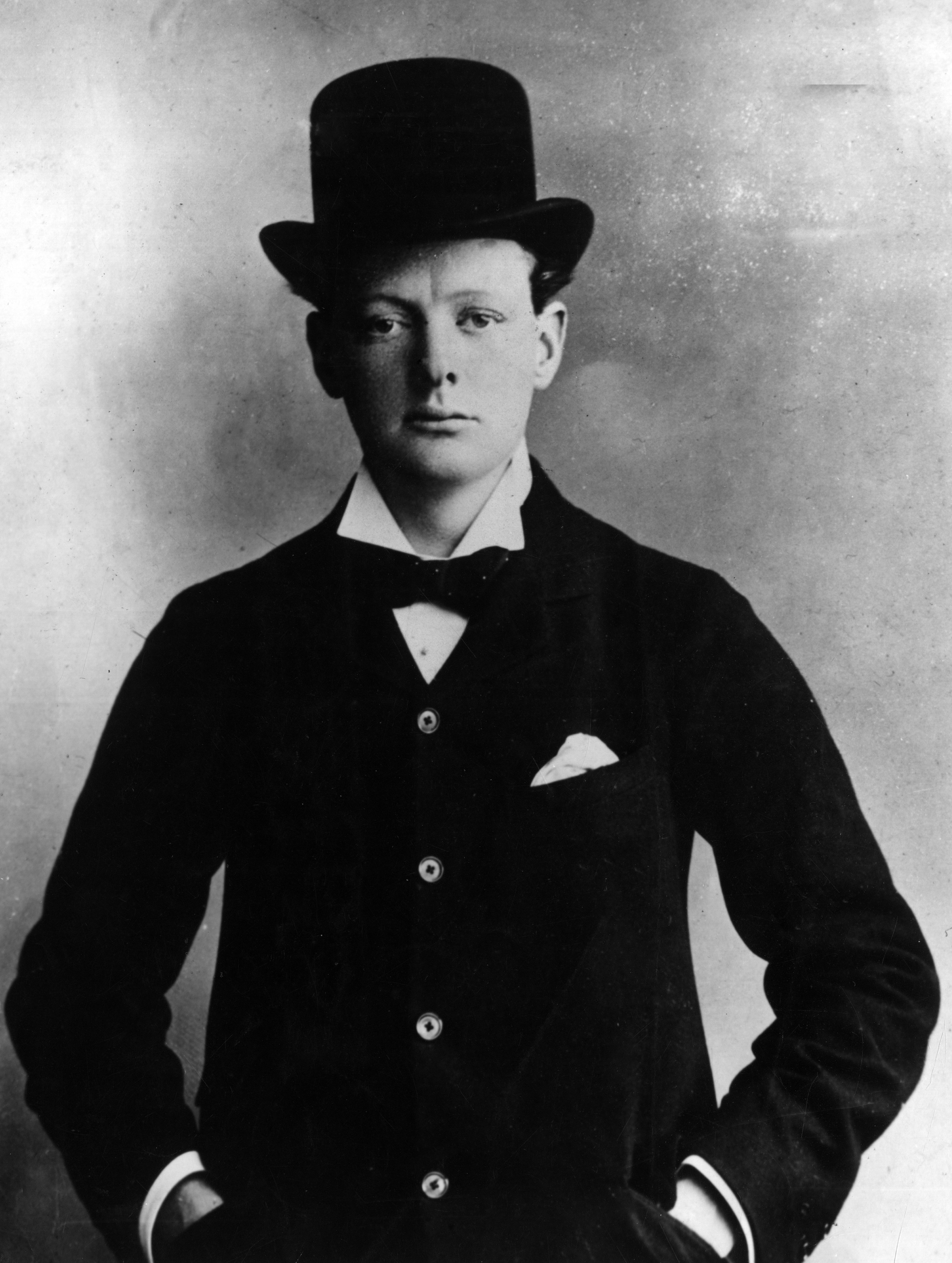 Young Winston Churchill in a formal suit and bowler hat stands with hands in pockets, posing for a portrait