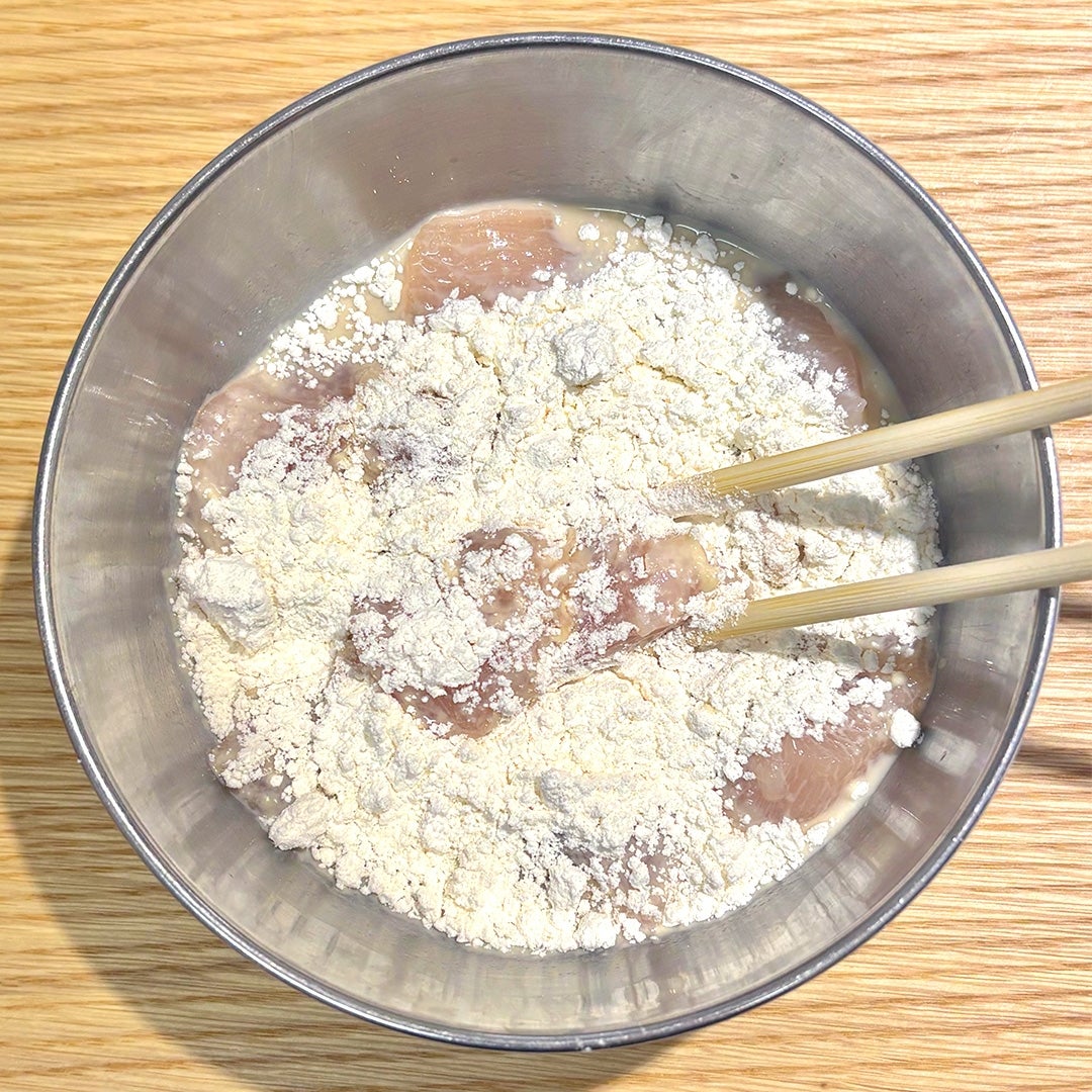 ボウルに鶏肉と小麦粉が入っており、箸で混ぜられている様子。