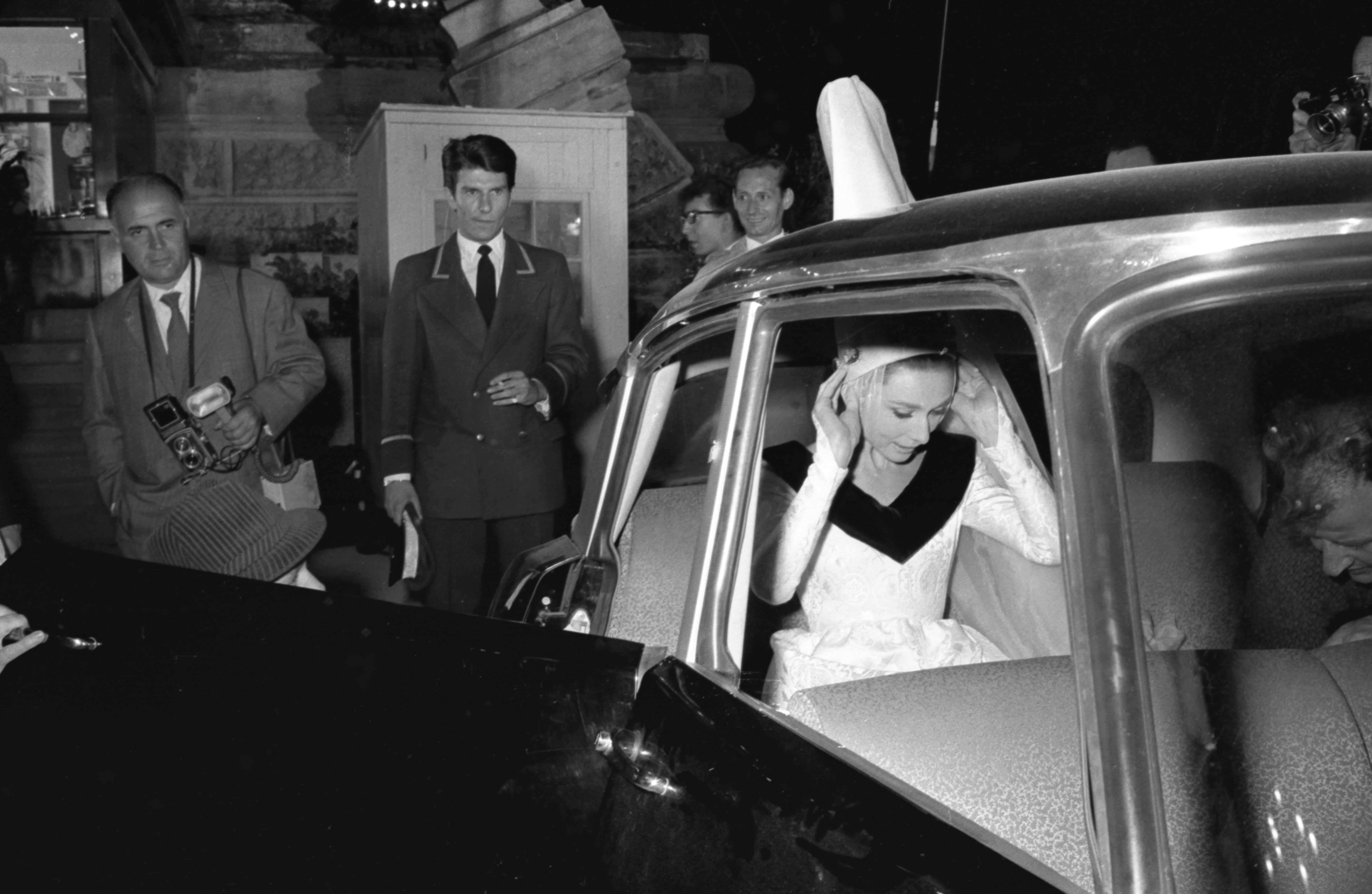 Audrey Hepburn adjusts her headpiece as she exits a car surrounded by onlookers at an event