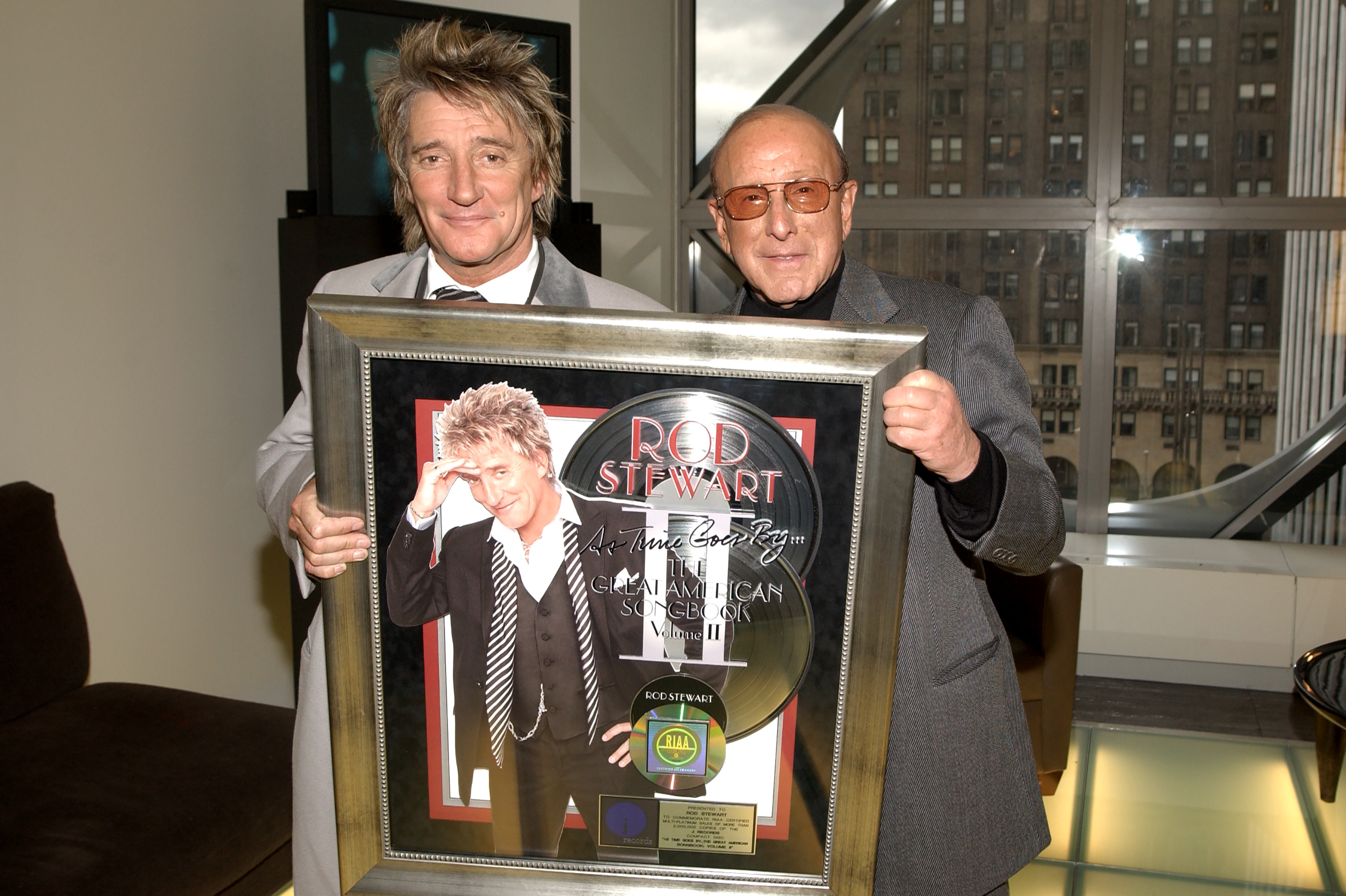 Two men are holding a framed plaque celebrating achievements. The image is used in an article categorized as LGBT