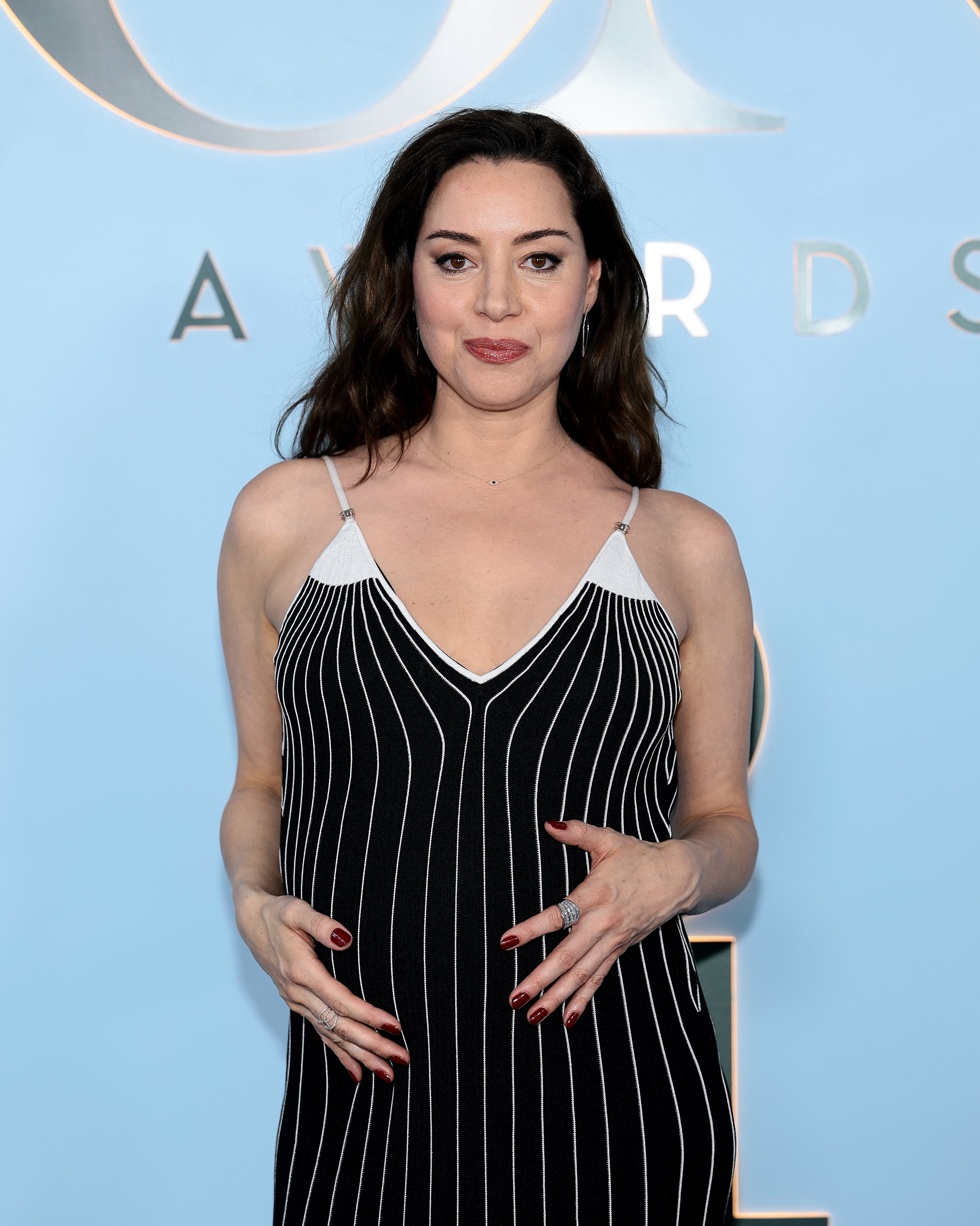 Person in a striped gown on a red carpet, posing with hands gently placed on the dress