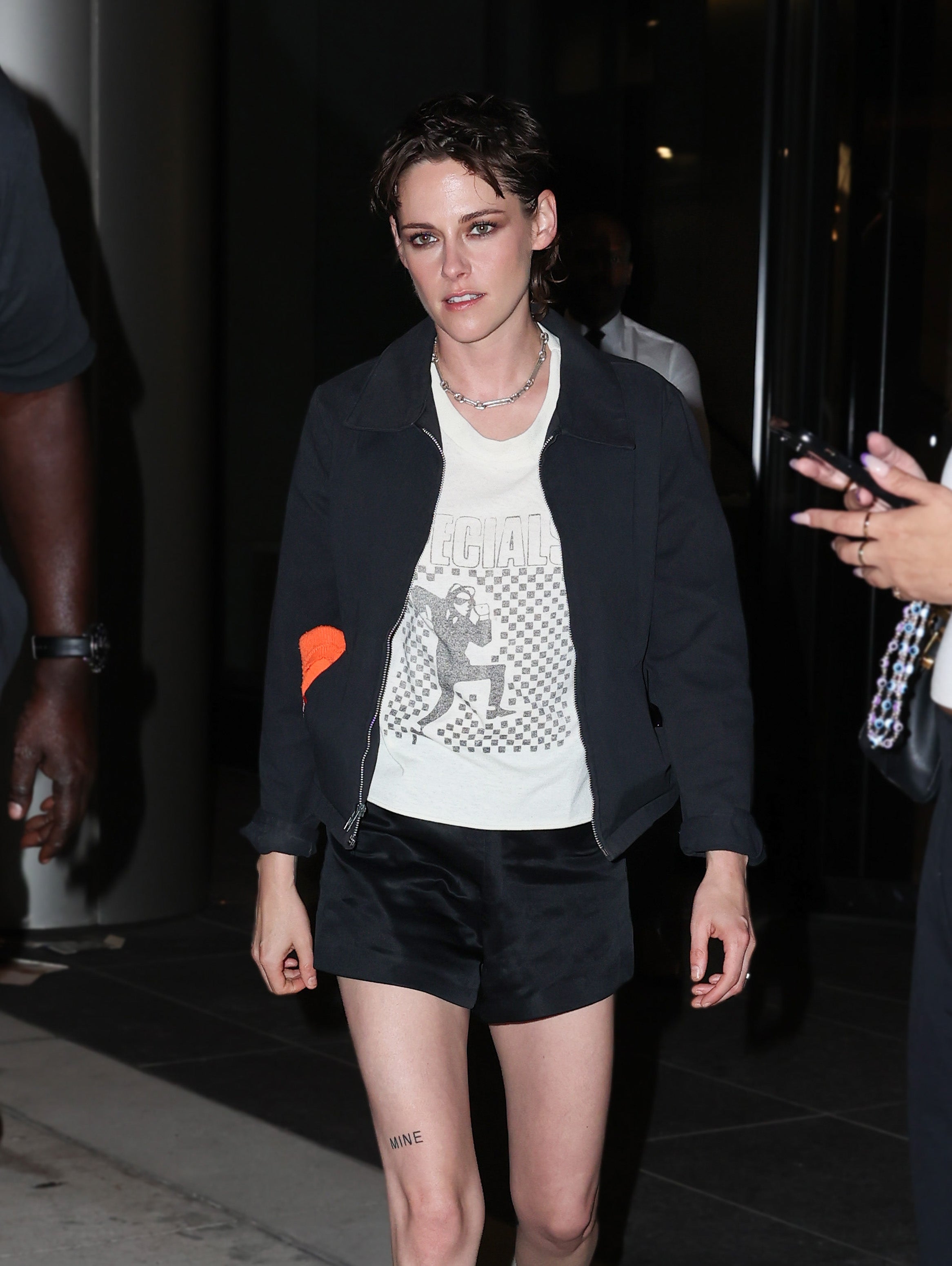 Person wearing a casual jacket, T-shirt with graphics, and shorts, photographed at a public event