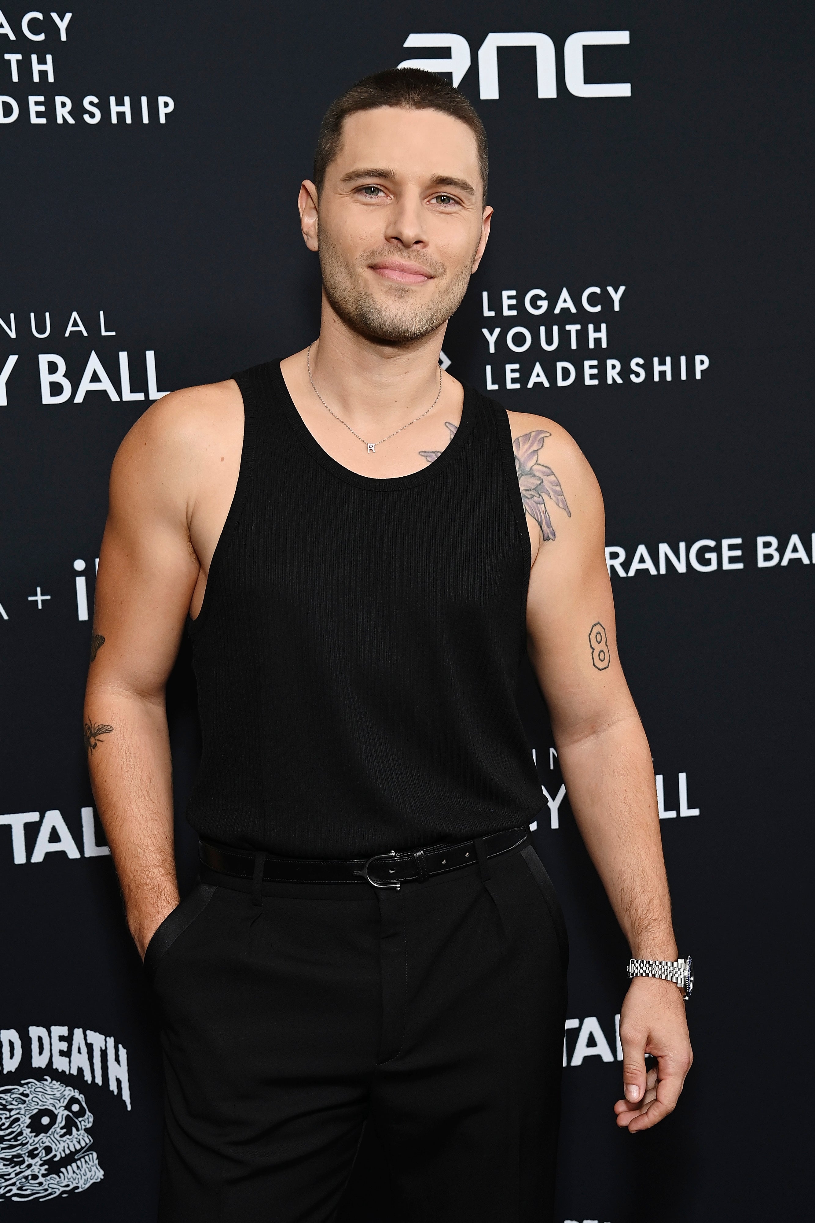 Person on a red carpet in a sleeveless top and pants, featuring tattoos. The event backdrop mentions legacy and leadership themes
