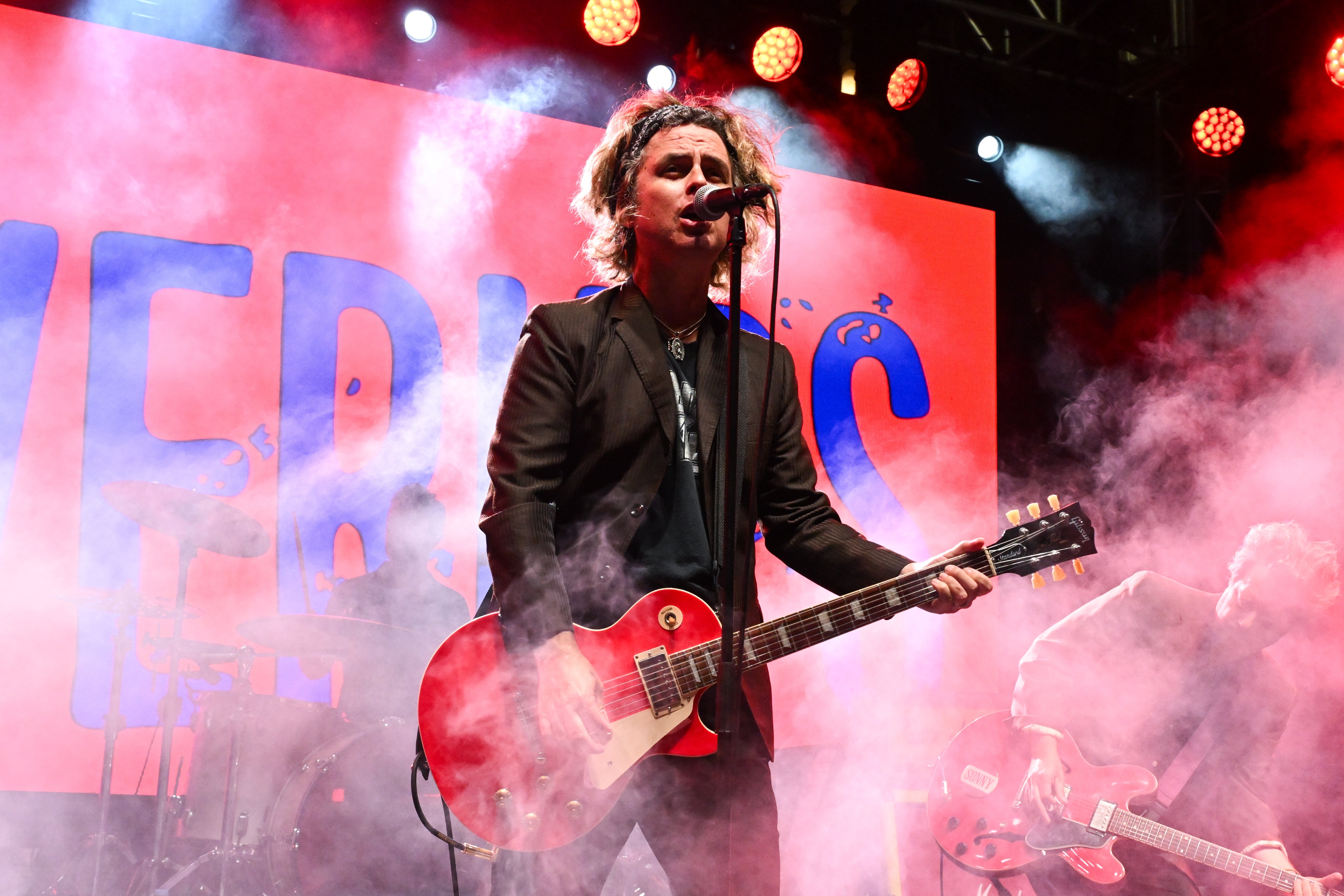 Musician performing on stage with a guitar, surrounded by colorful lights and fog effects