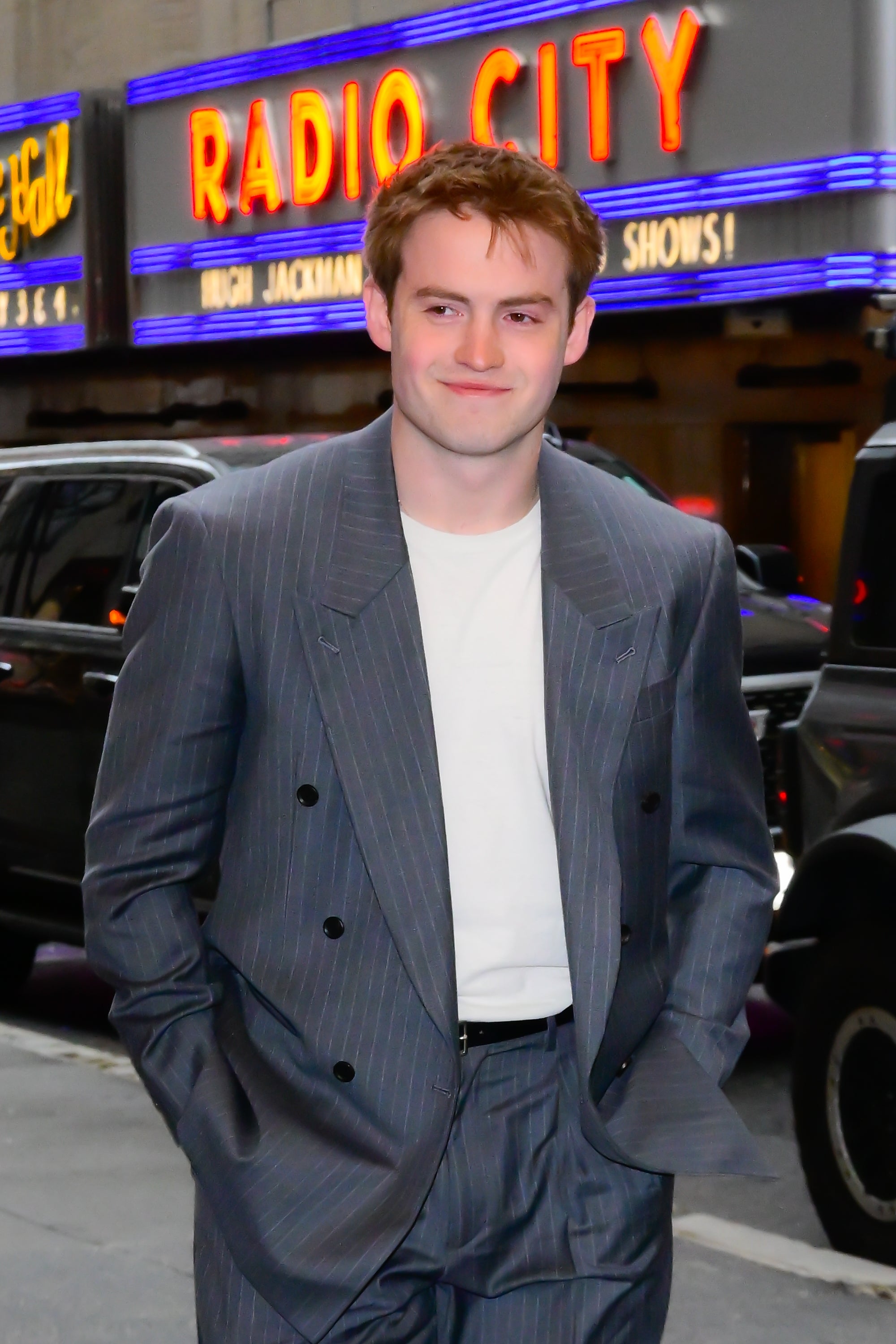 Person in a striped suit and white shirt walking near Radio City Music Hall signs