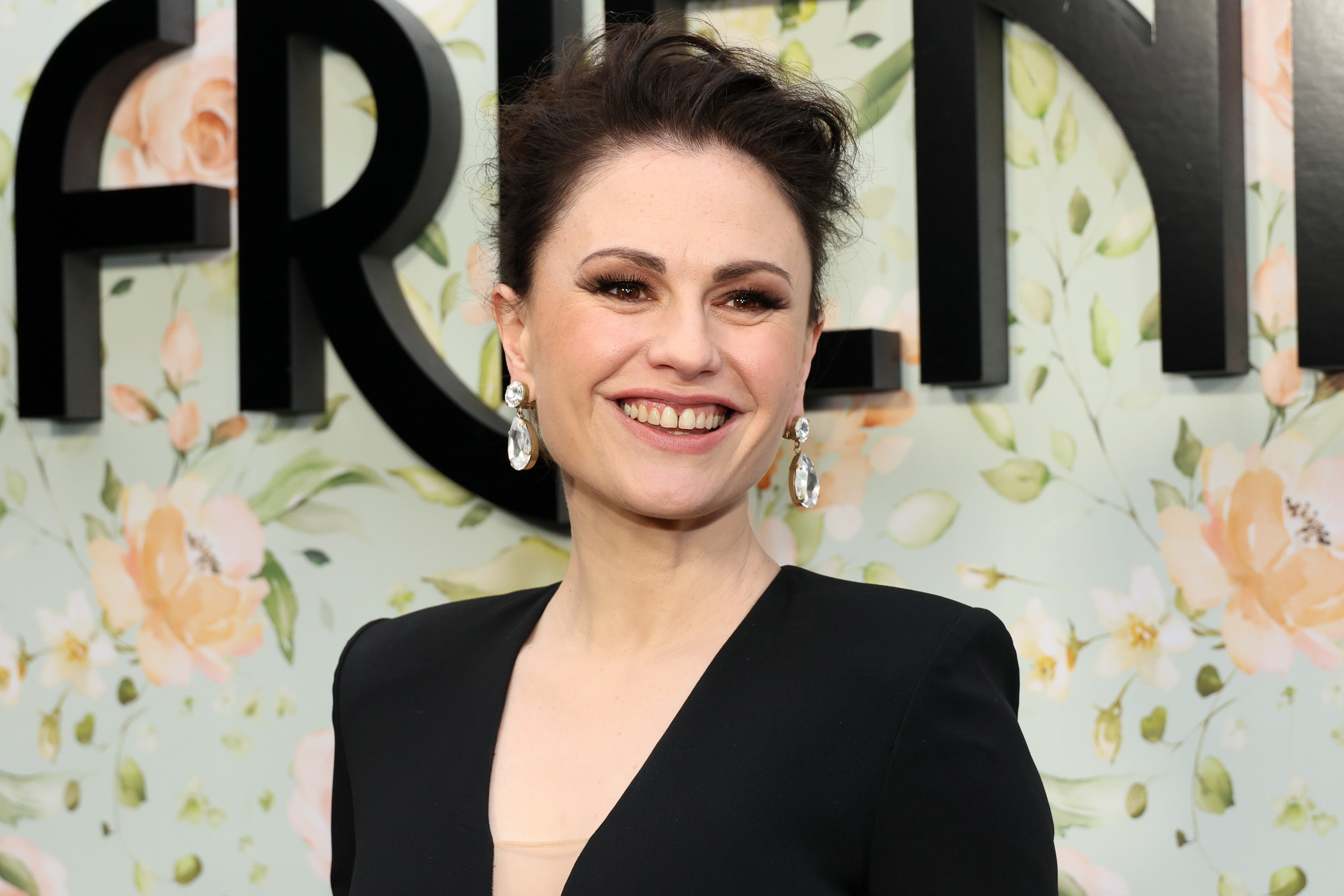 Person smiling in elegant black dress with floral background at event