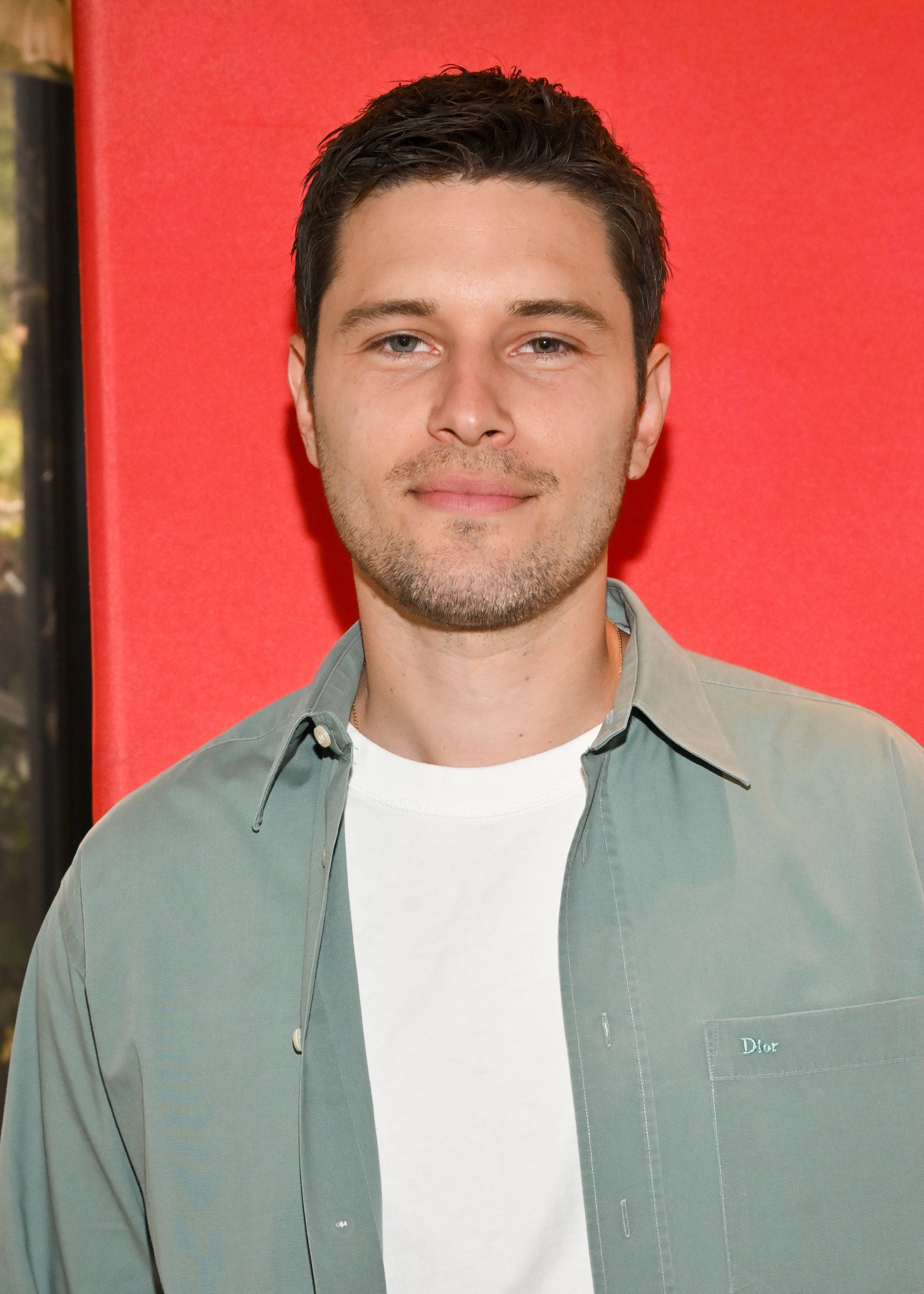 Person in a casual shirt stands against a plain backdrop, looking into the camera