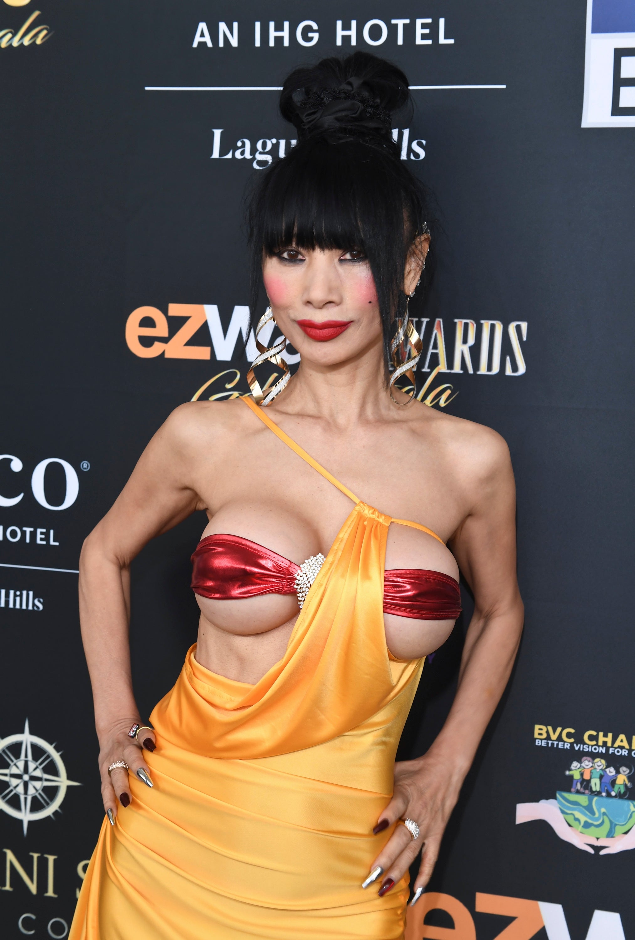 Person in a striking dress with an asymmetrical style at a red carpet event, posing confidently