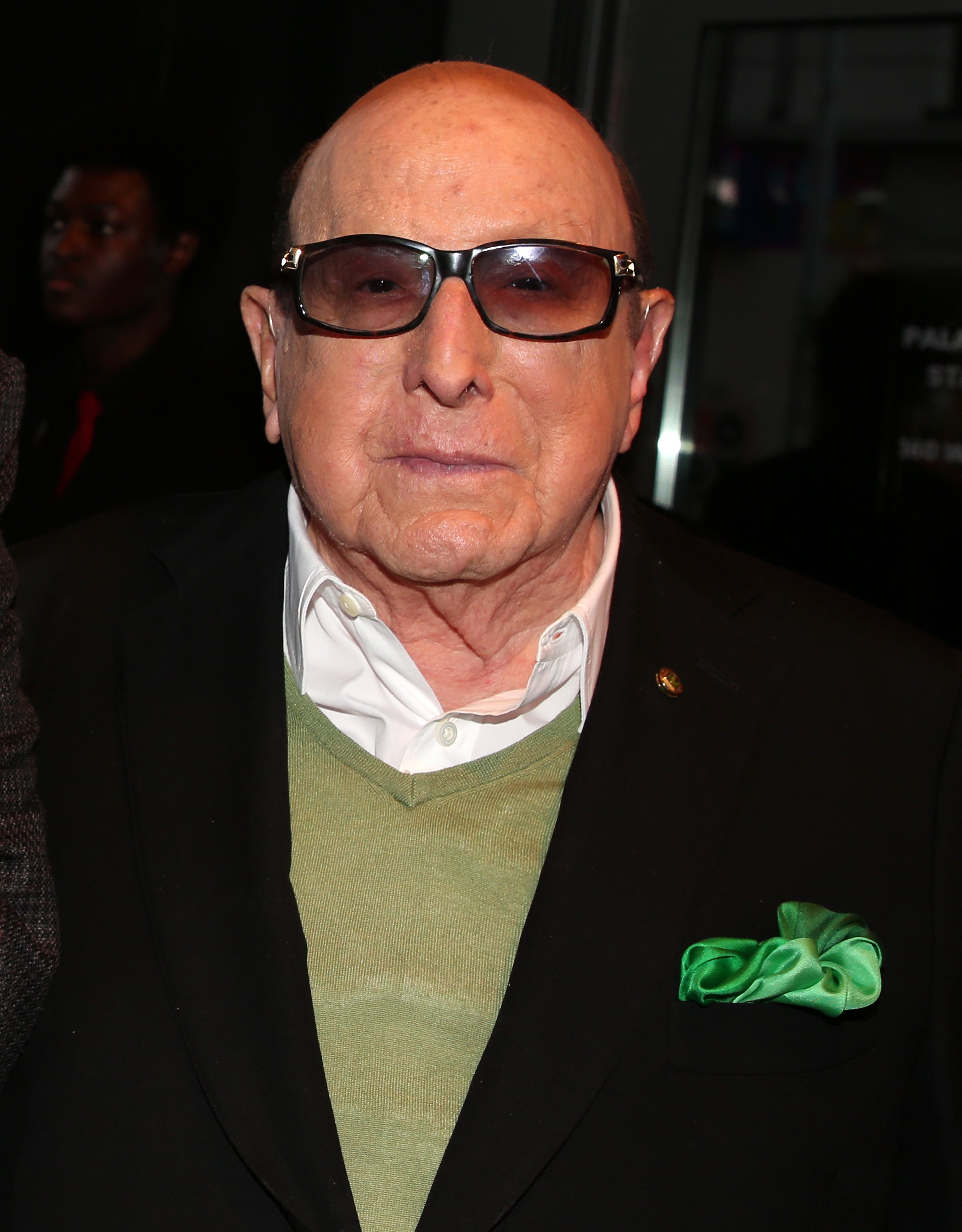 I don't know who this is. The person is wearing sunglasses, a green sweater under a dark suit, and a green pocket square