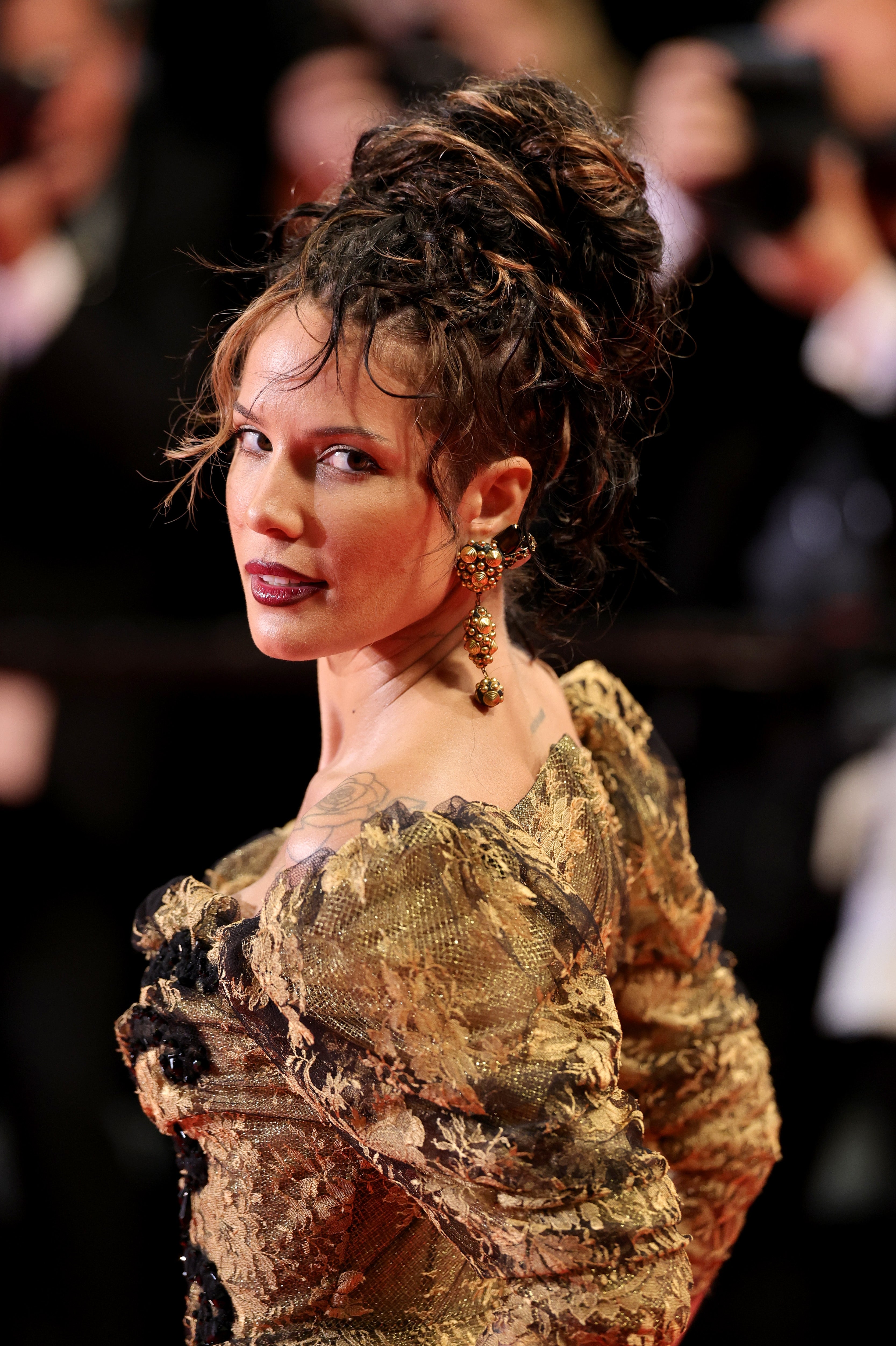 Person on red carpet in textured, high-neck gown with intricate details, styled hair, and statement earrings, posing confidently