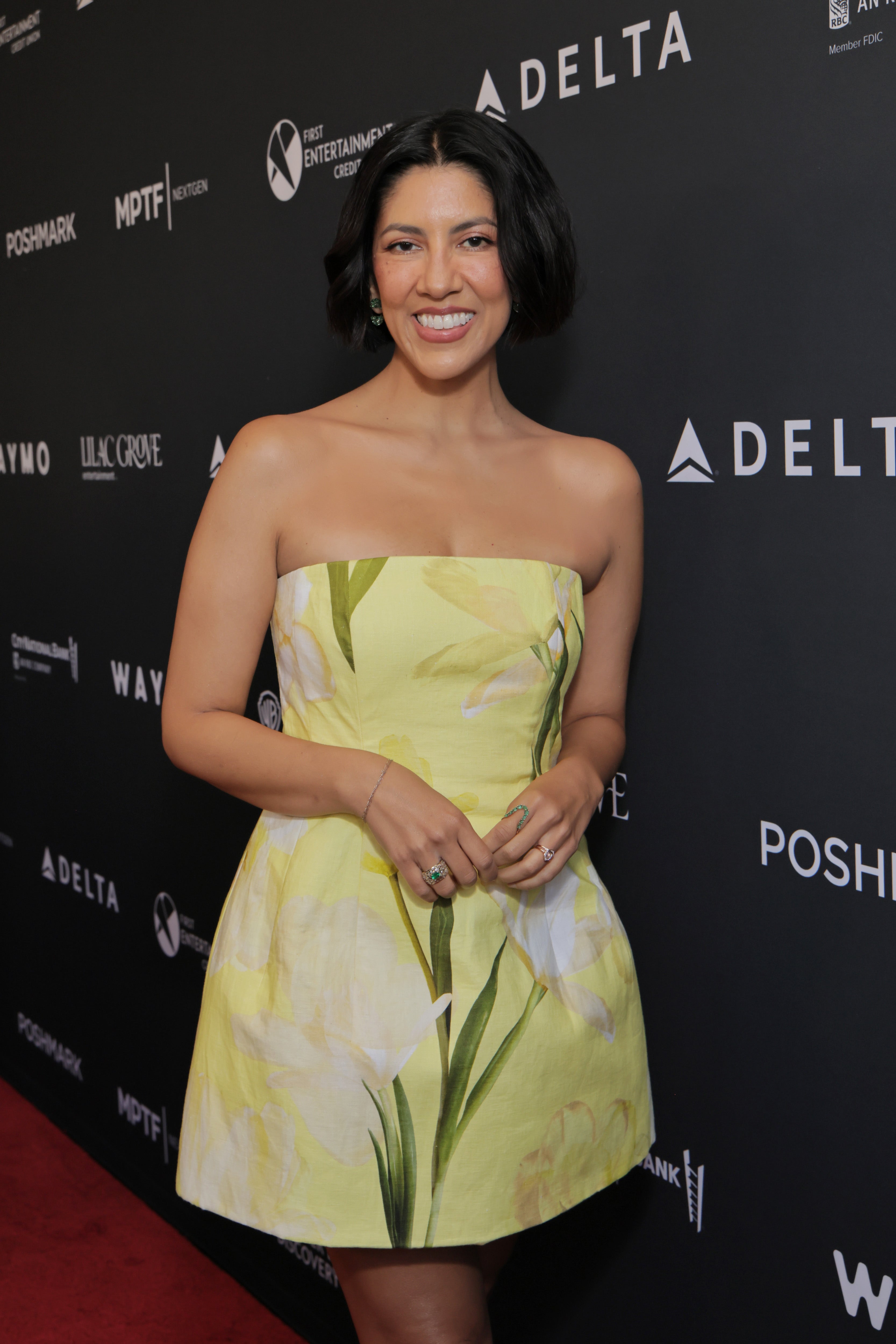 Person in floral strapless dress smiles on the red carpet at an event