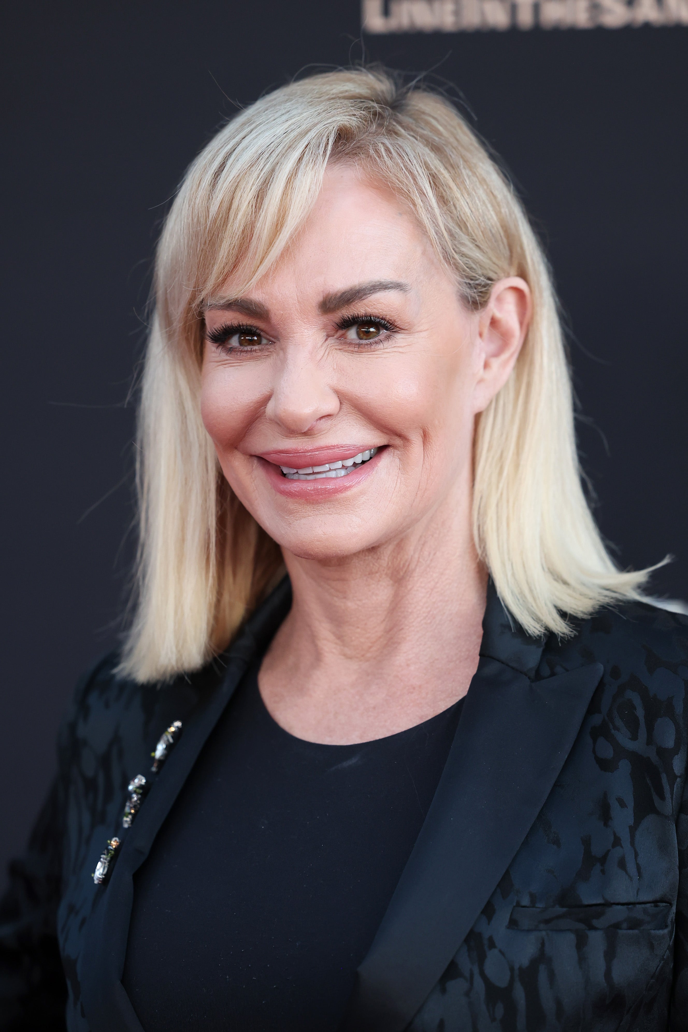 Person smiling on a red carpet in a black patterned jacket and top