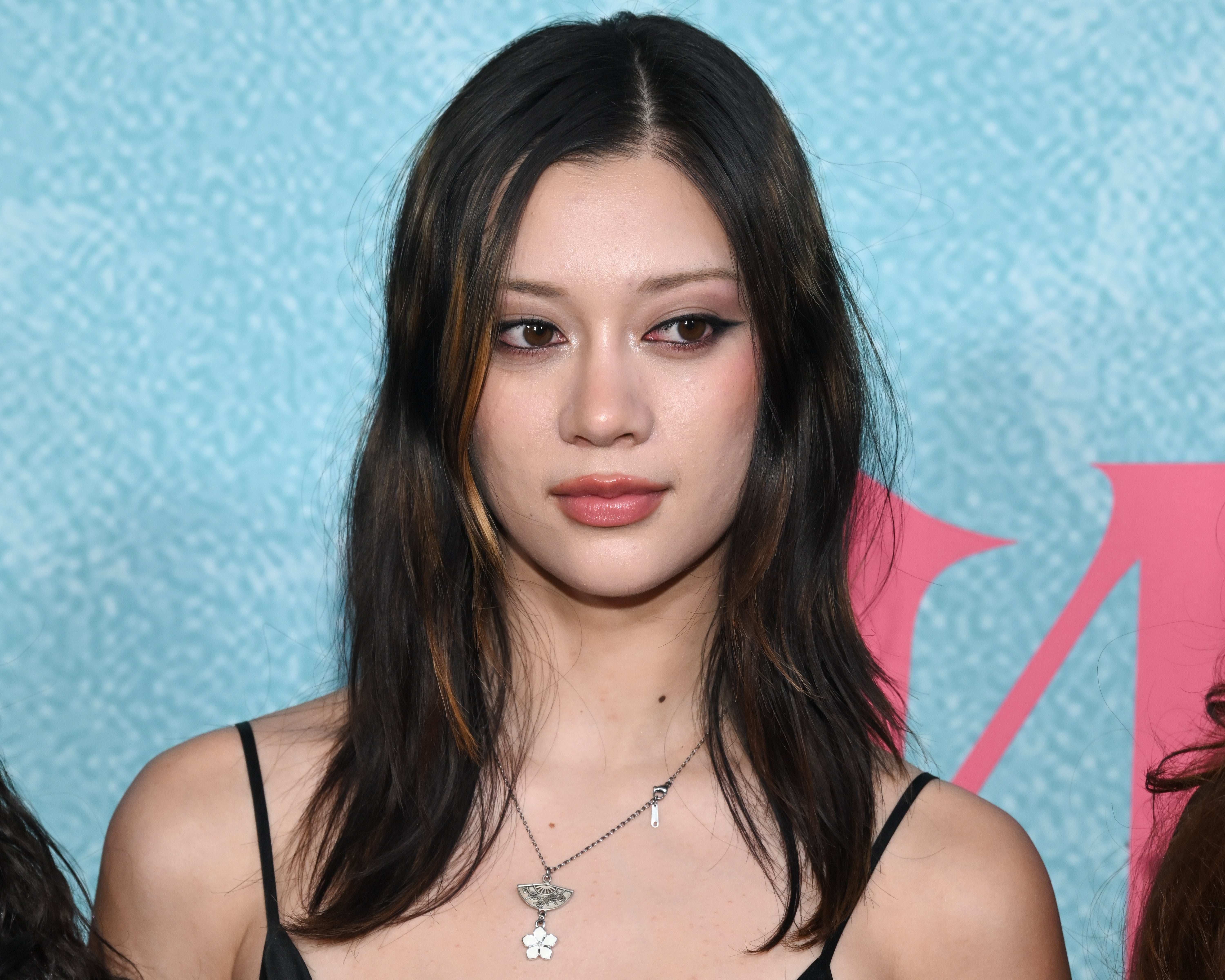 Person with long hair wears a necklace and a stylish black top, posing at a public event