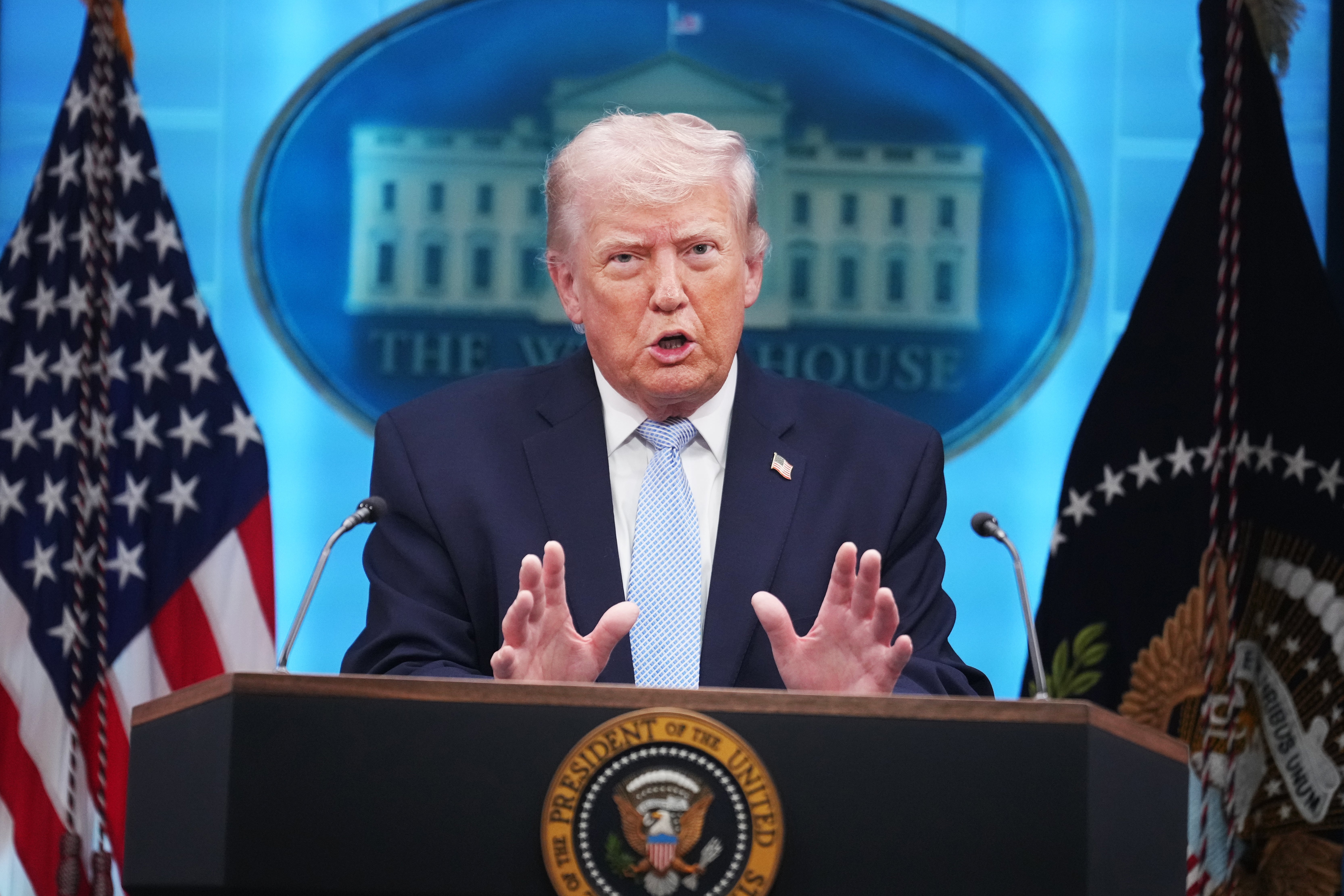 En person på et podium foran Det hvite hus i bakgrunnen under en pressekonferanse, med det amerikanske flagget og presidentstempelet synlig