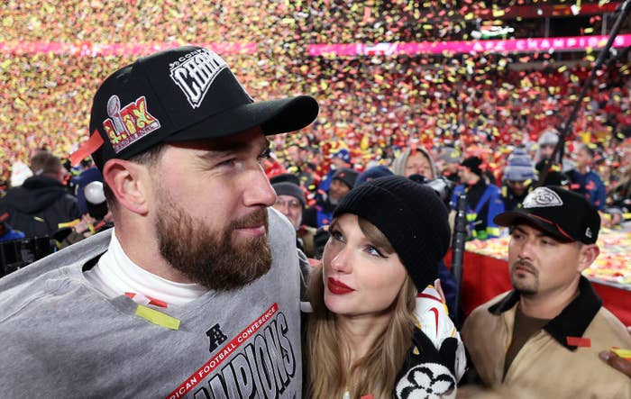 A football player in a championship shirt and hat is embraced by a woman in a stylish beanie amidst confetti on a sports field