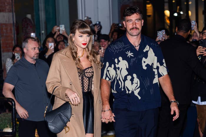 I don't know who these people are, but the woman is wearing a lace top, leather skirt, and trench coat, holding hands with a man in a patterned shirt