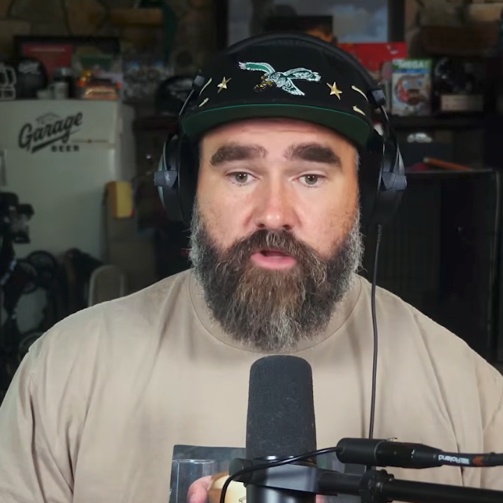 Two men with headphones and microphones appear in a podcast video call. One is bearded and serious, while the other is smiling