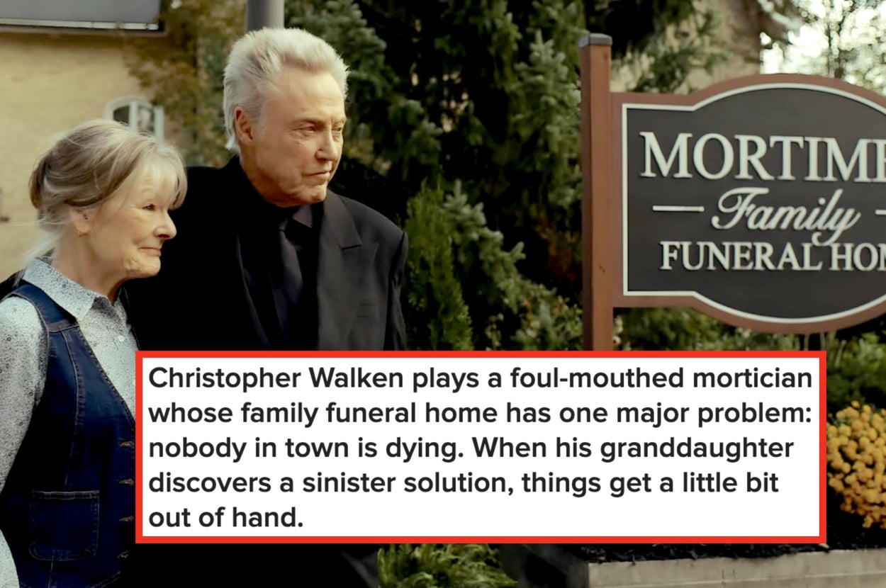 Two individuals stand outside Mortimer Family Funeral Home, with greenery and flowers around them