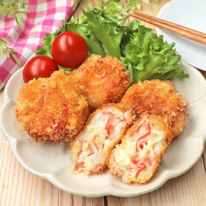 皿に盛り付けられた揚げ物のカニクリームコロッケとトマト、レタスの付け合わせ。