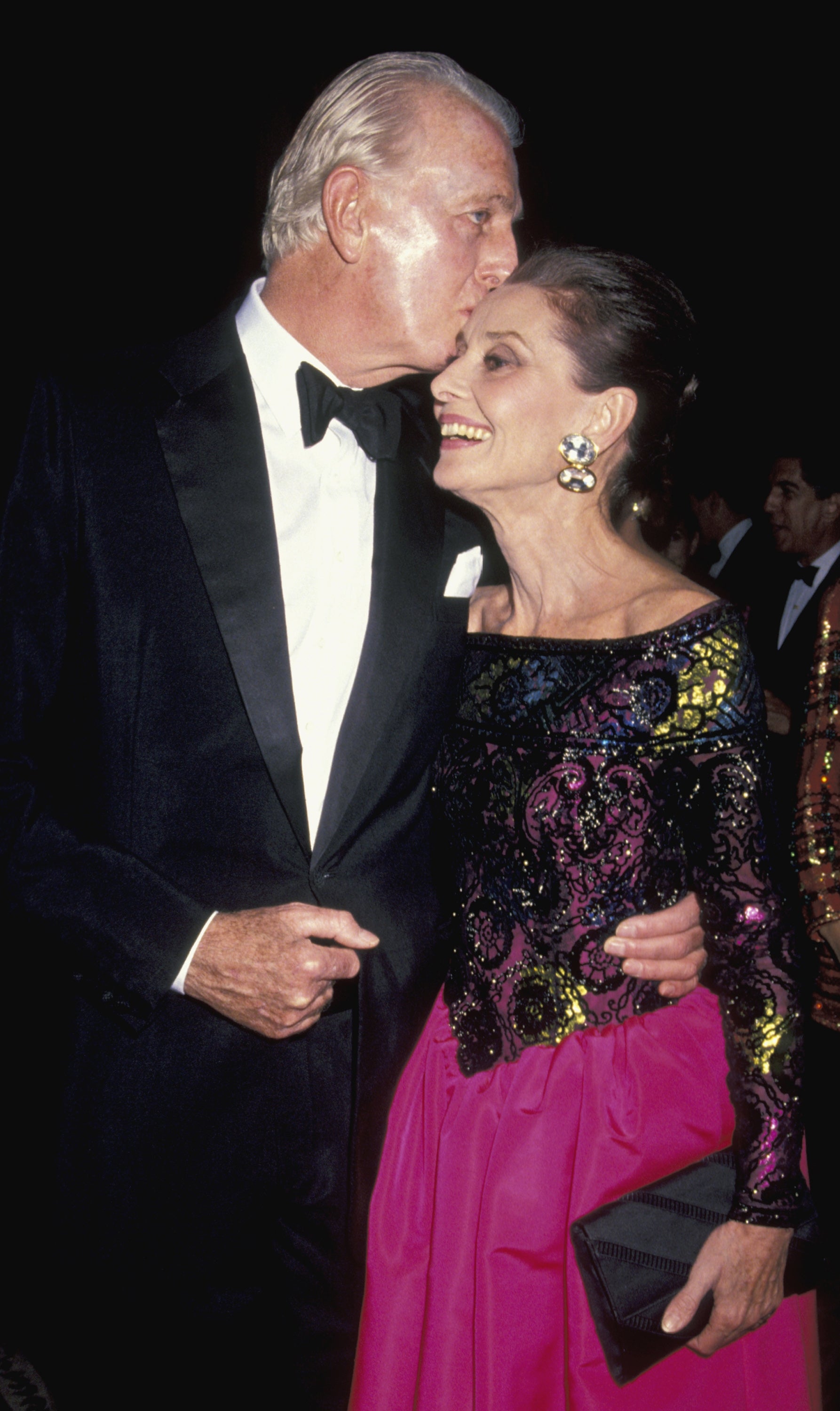 Givenchy in a tuxedo kisses Audrey in an elegant sequined top and long skirt on the head, posing at a formal event