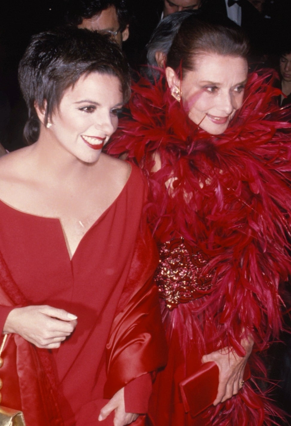 Audrey Hepburn and Liza Minelli on a red carpet in elegant red evening attire, with cameras capturing the moment