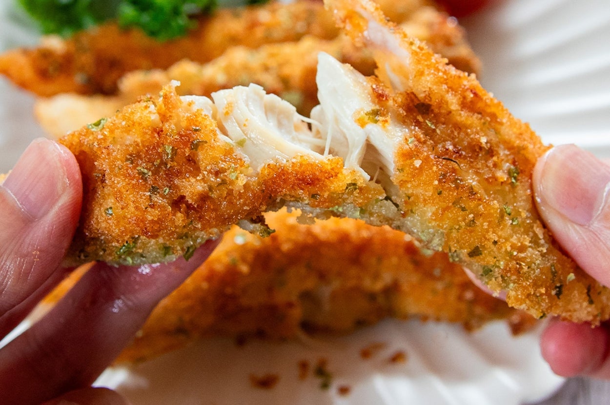 手で裂かれる衣付きのチキン。後ろに彩りを添えるトマトとパセリ。