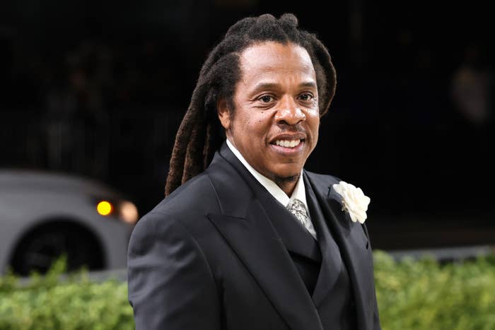 A person in a formal suit with a floral boutonniere smiles at a public event