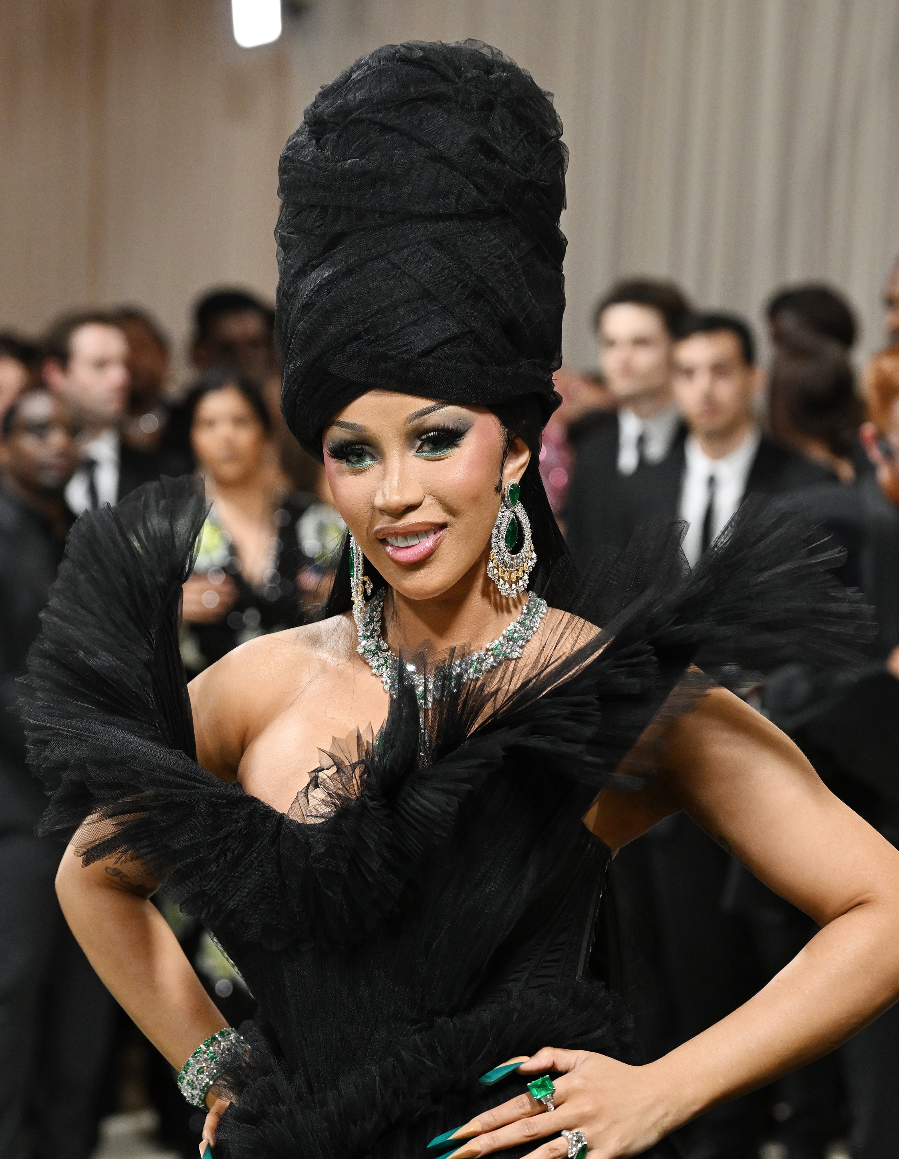 Person in a dramatic gown with a large head wrap, lavish jewelry, and confident pose at an event