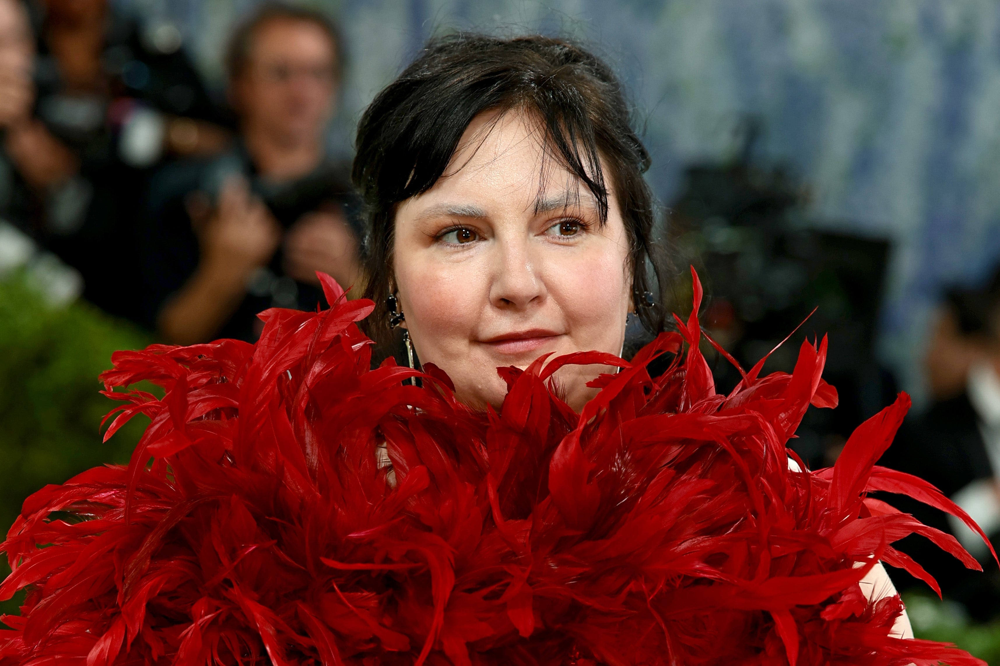 A person on a red carpet is partially obscured by extravagant, feathered attire