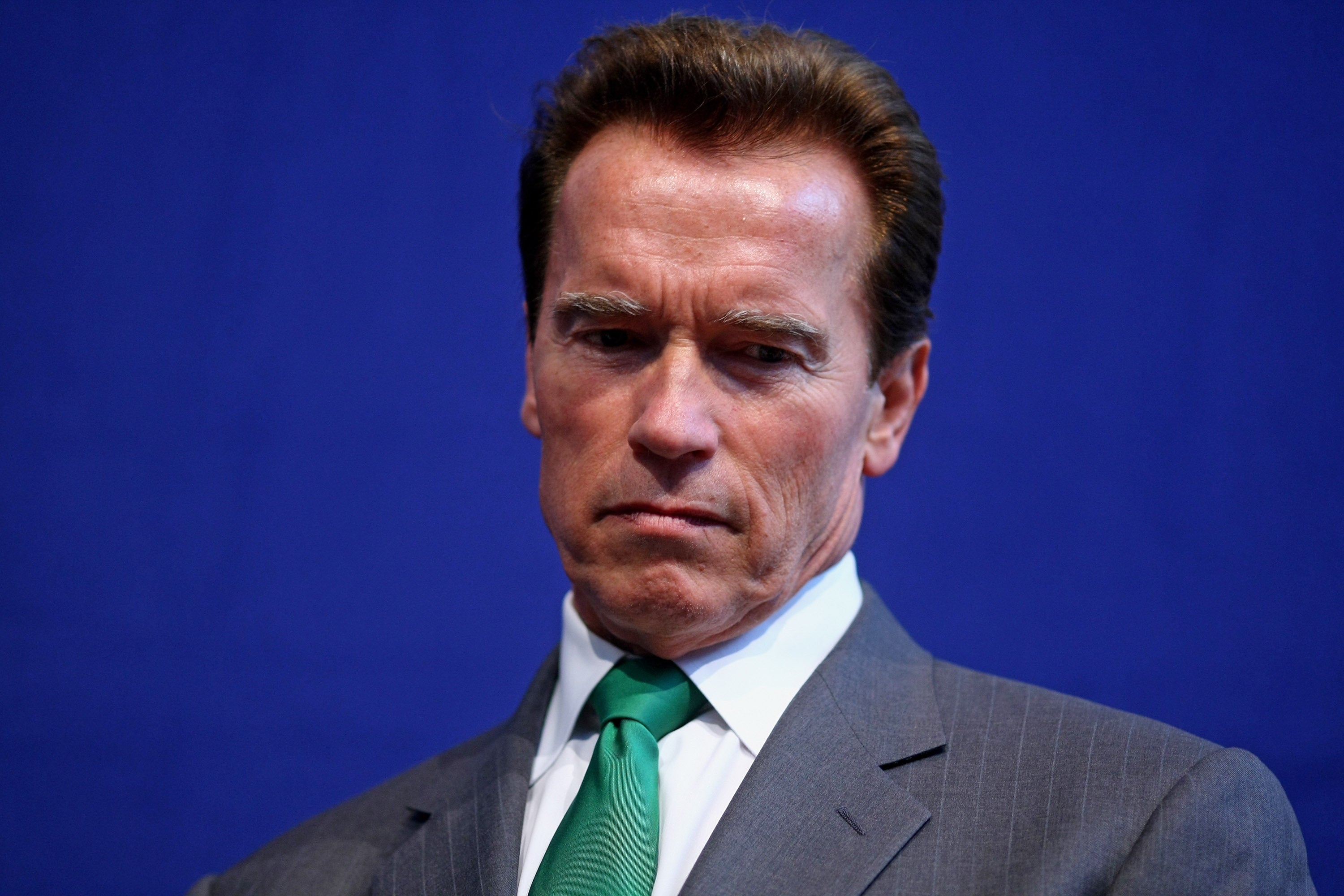 A man in a suit and tie against a solid background, looking thoughtful