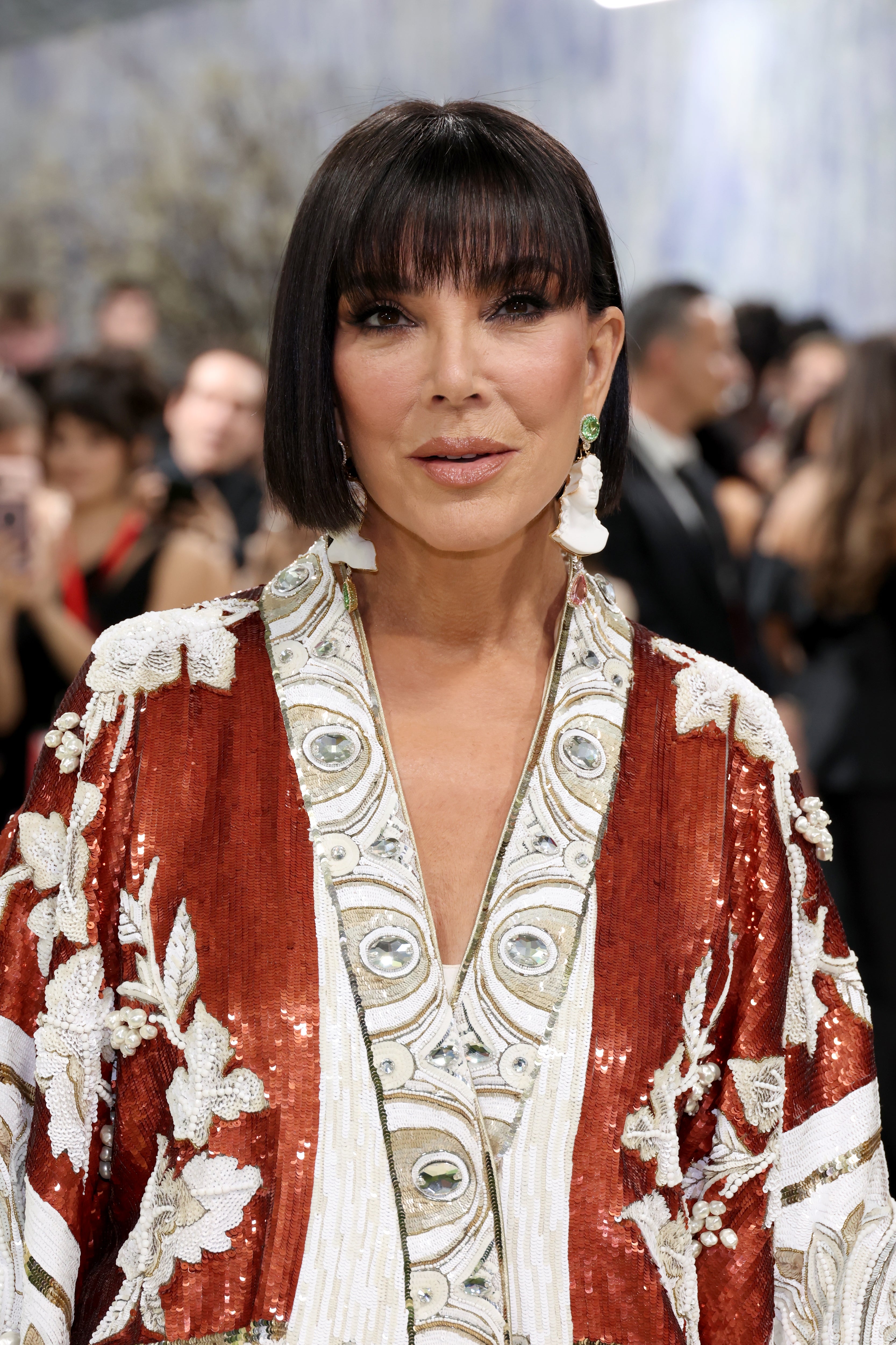 Person on a red carpet in a sequined robe with white floral patterns and fringe