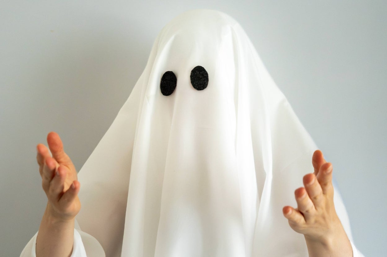Person dressed as a ghost with a white sheet and black eyes. Hands raised in front