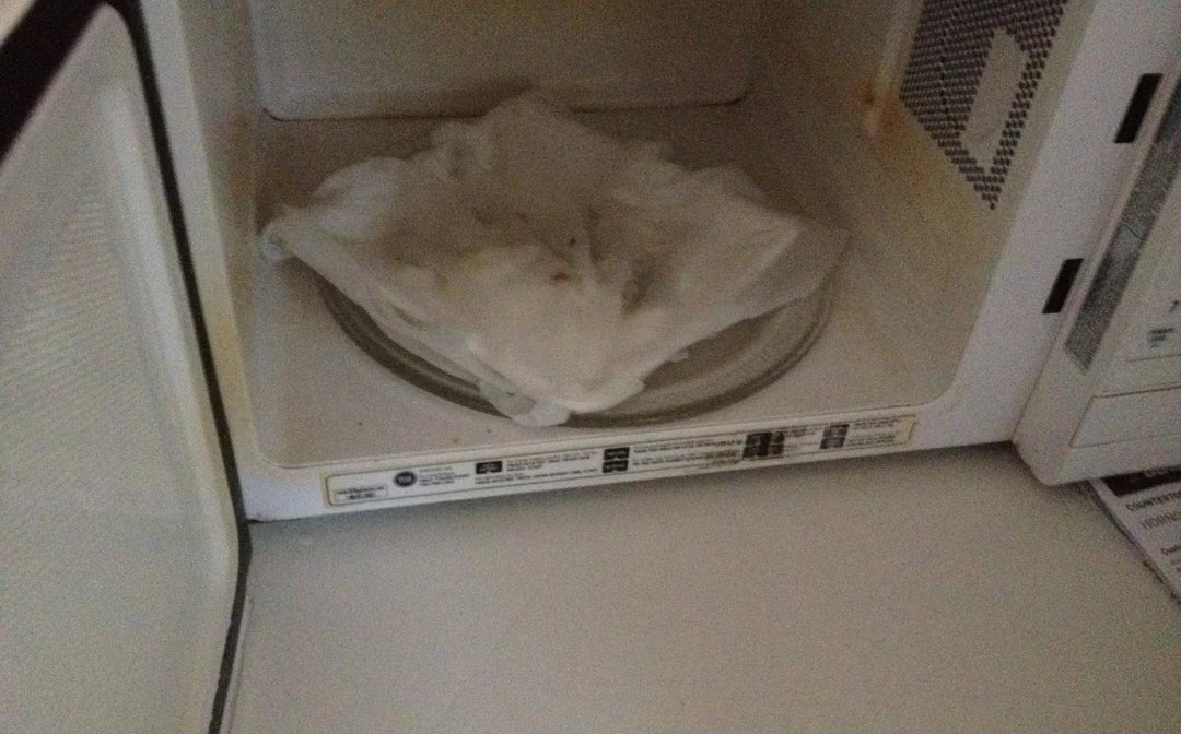 A microwave with a glass turntable covered in a steaming, crumpled paper towel, suggesting food warming or recent cooking mishap