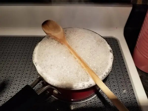 Pot on stove with water boiling over, wooden spoon on top to prevent spills