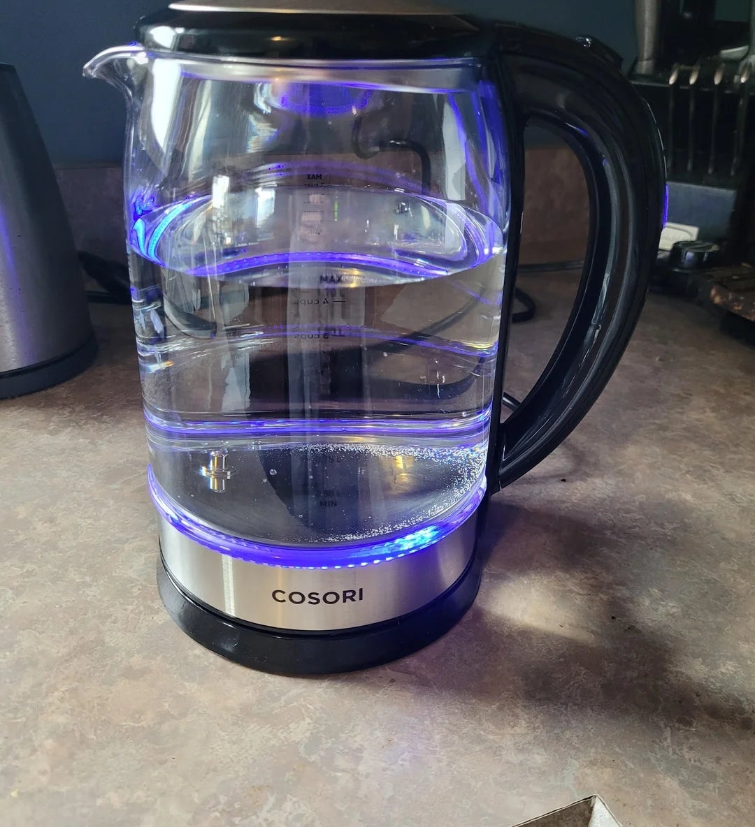Electric kettle on a kitchen countertop, partially filled with water, featuring a blue light indicator