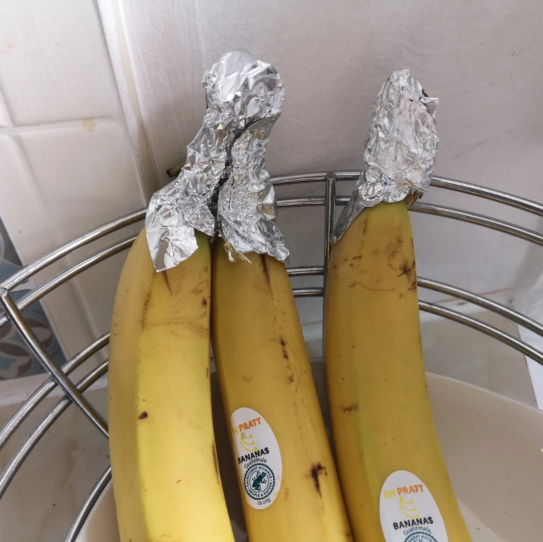 Bananas with foil wrapped around their stems in a kitchen bowl