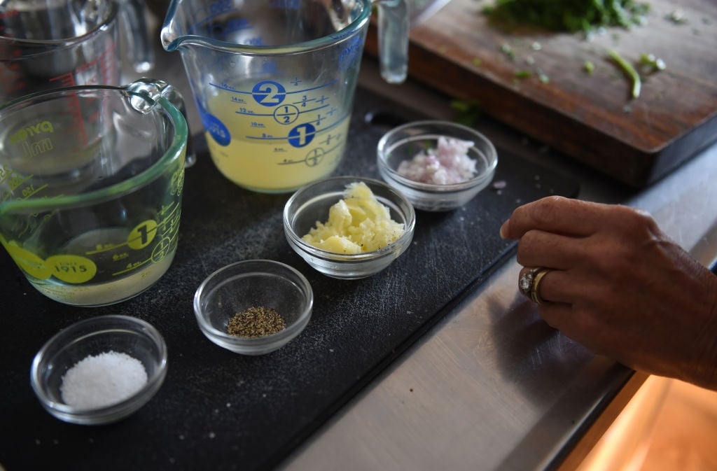 Various small bowls on a cutting board contain ingredients like minced garlic, chopped shallots, lemon juice, salt, and pepper