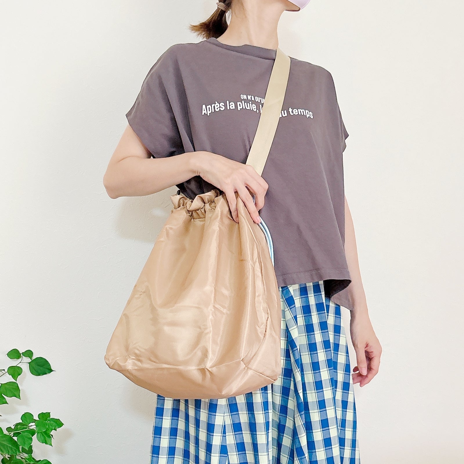 3COINS（スリーコインズ）の「たためる巾着エコバッグ／ENJOY PARK」斜め掛けで持っている様子。