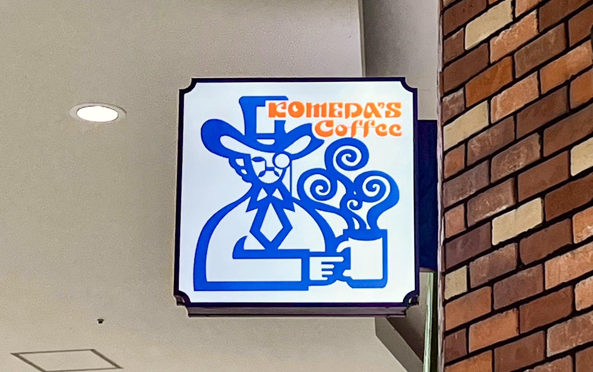 喫茶店「コメダ珈琲店」のロゴ看板が店の外壁に掲げられている。帽子と髭の男性イラスト。